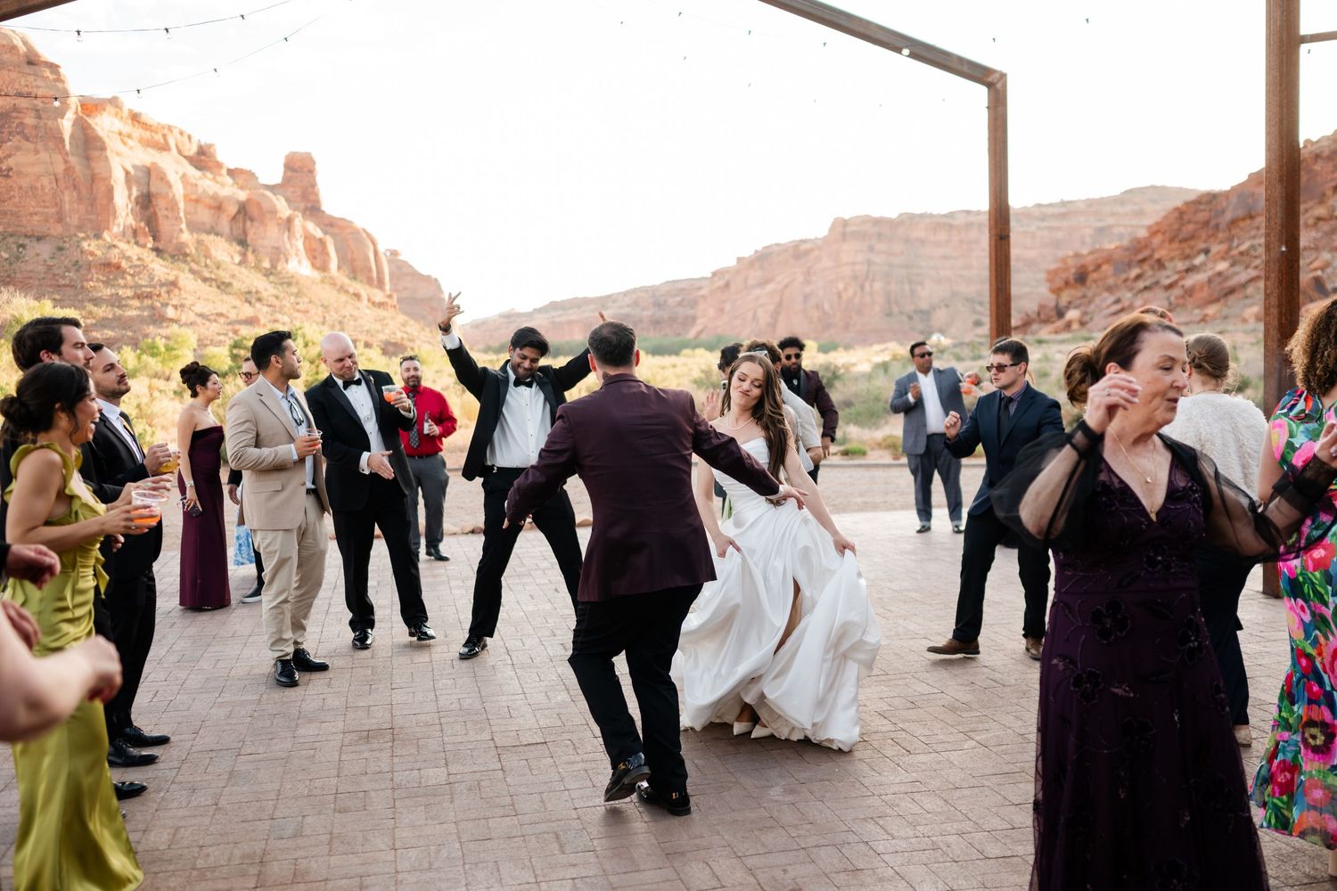 Bride and groom dance joyfully at outdoor wedding reception with red rock canyon backdrop in Moab, Utah.