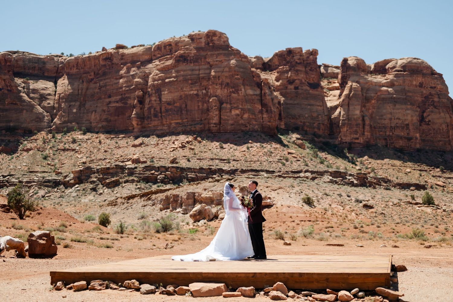 Couple exchanging vows on a wooden platform in a stunning red rock desert landscape.