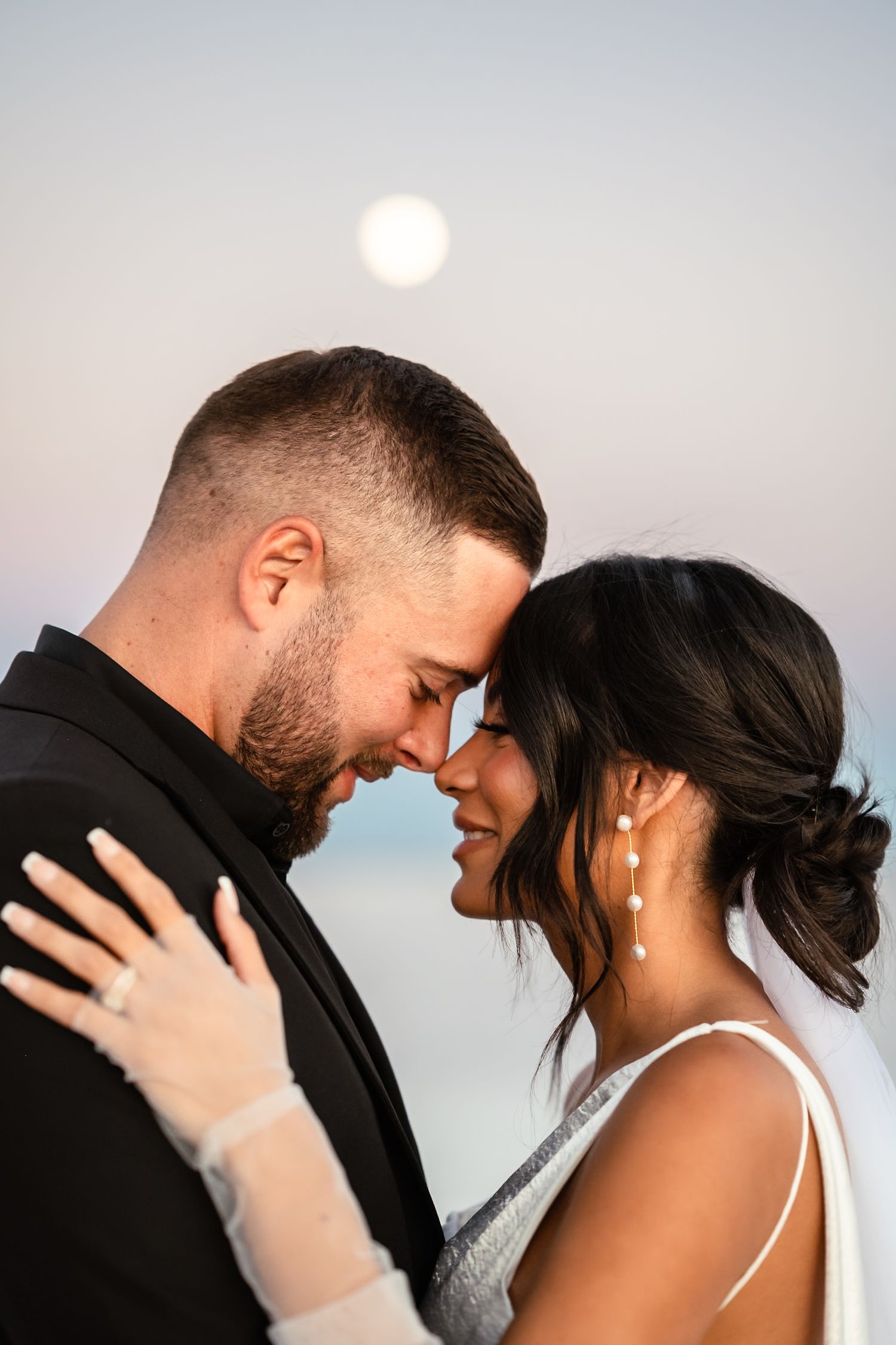Romantic couple shares an intimate moment against a soft sunset sky.