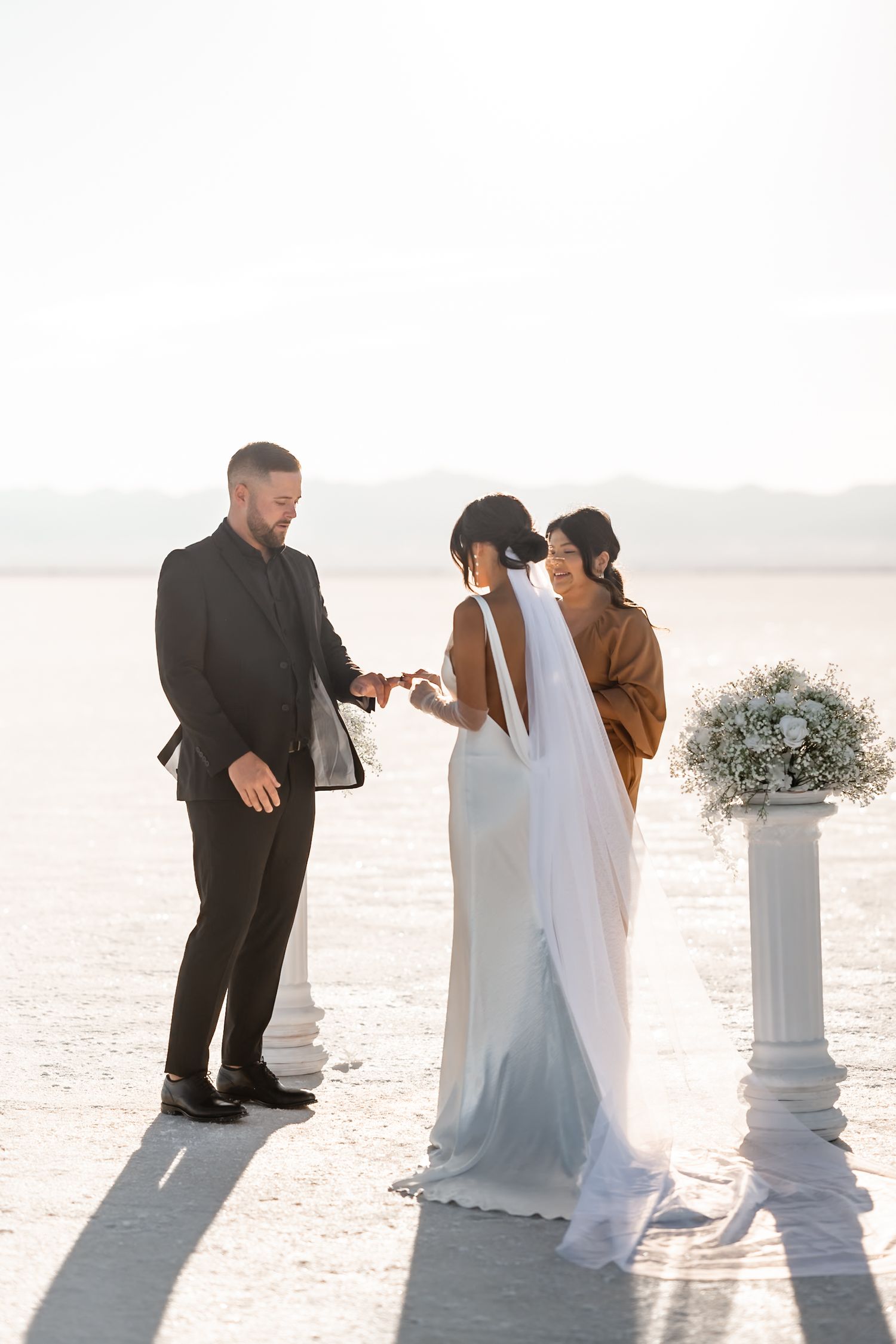 A sequence of romantic wedding photos showing a couple dancing together on a white salt flat during sunset.