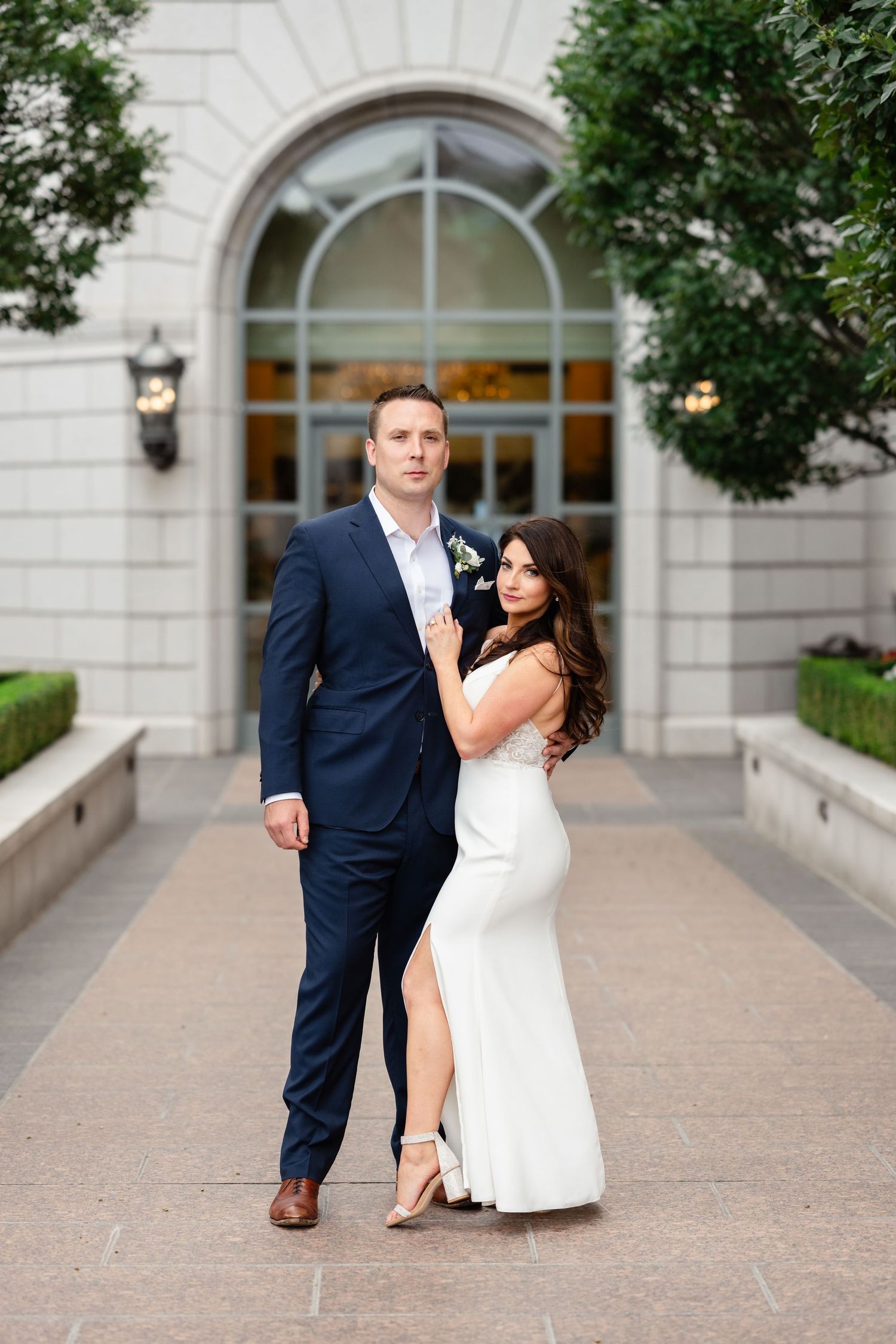 Couple in wedding attire poses together in a series of romantic shots under an elegant stone archway. Grand America Hotel micro wedding.