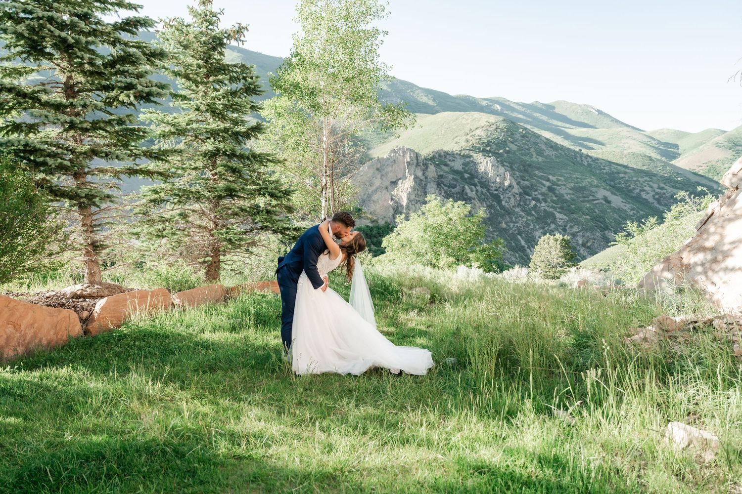 A couple sits together on a grassy hillside overlooking scenic mountain views on a sunny summer day. Louland Falls Photographer.
