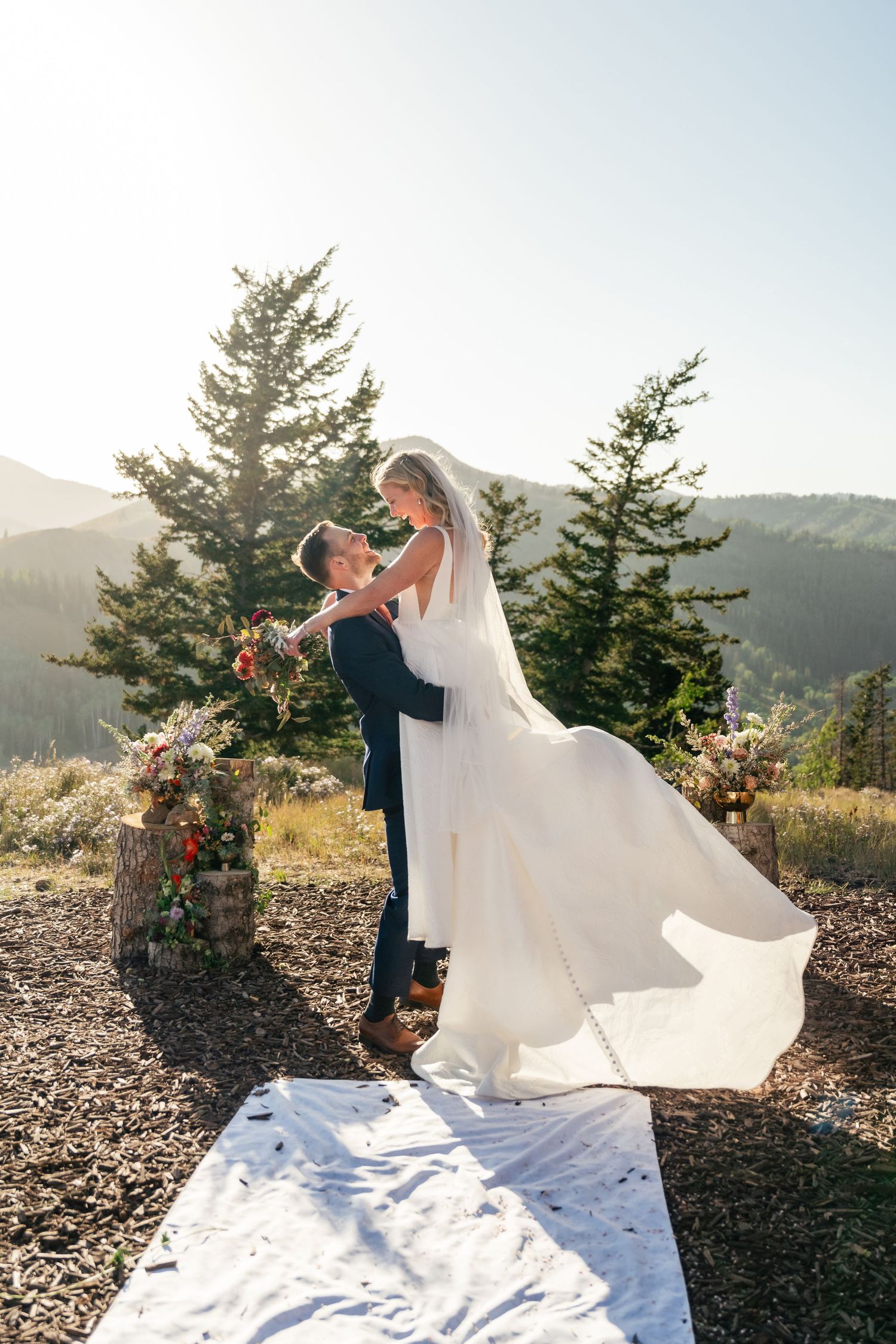 A couple shares a romantic moment in their wedding attire against a scenic mountain backdrop at sunset. Park City Wedding Photographer.