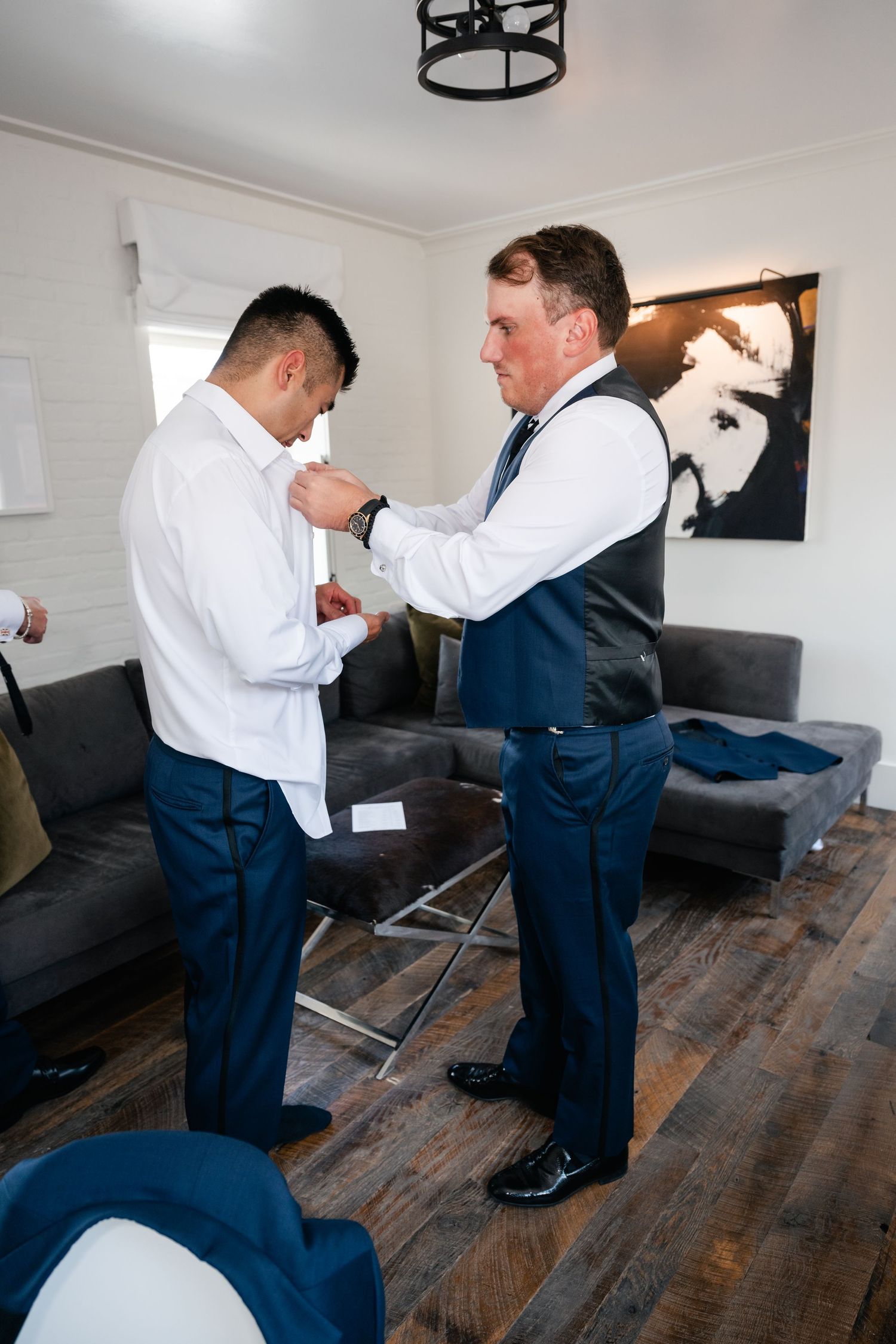 Two men helping each other with formal attire preparations in a modern living space.