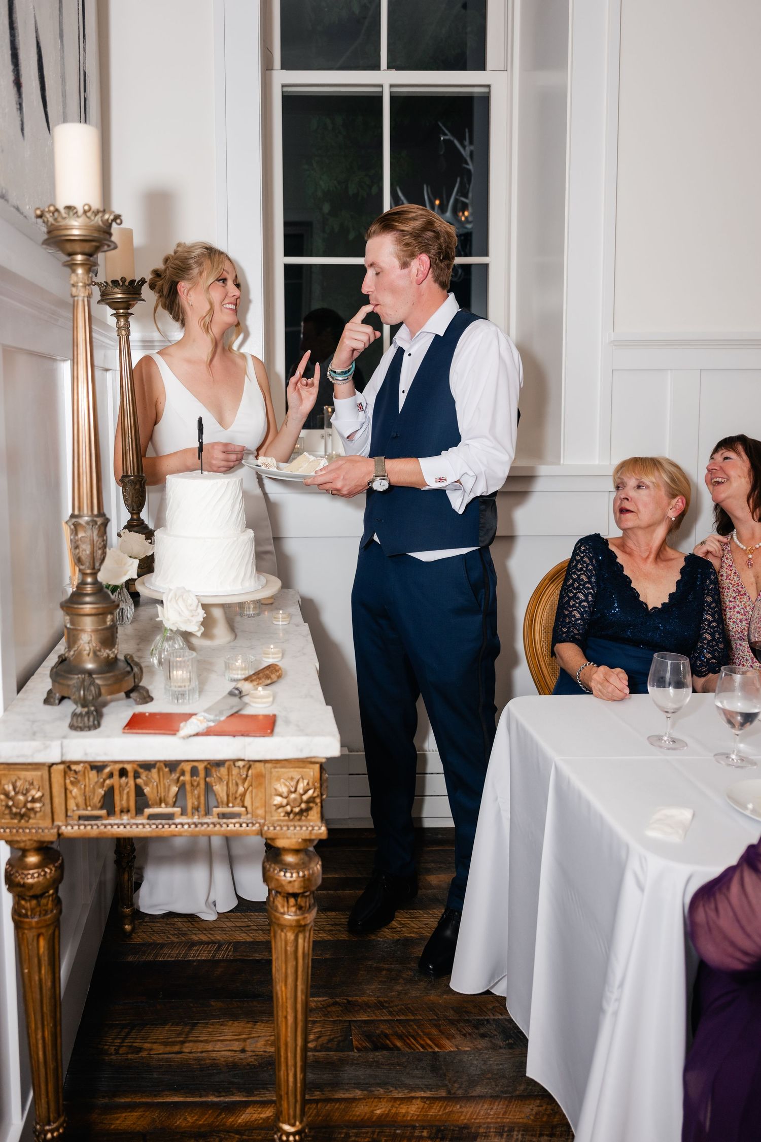 Wedding guests share joyful moments while cutting cake at an elegant indoor reception.