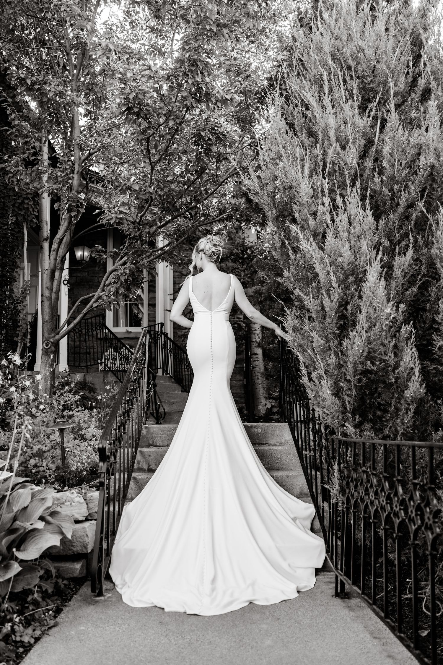 A stunning white wedding dress with a full skirt and train displayed in a garden setting with black iron railings.