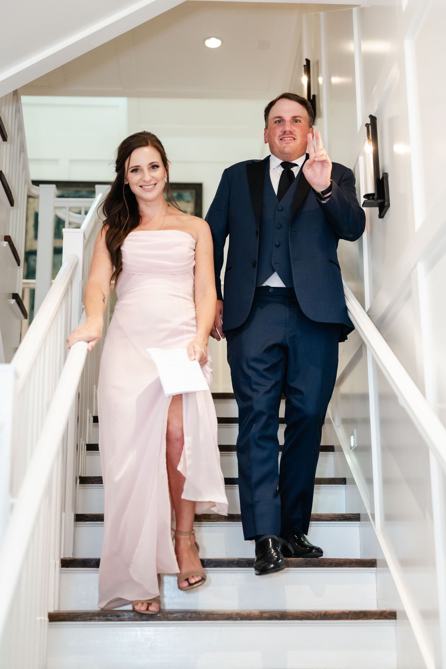 Couple descends white staircase in formal attire during wedding celebration.