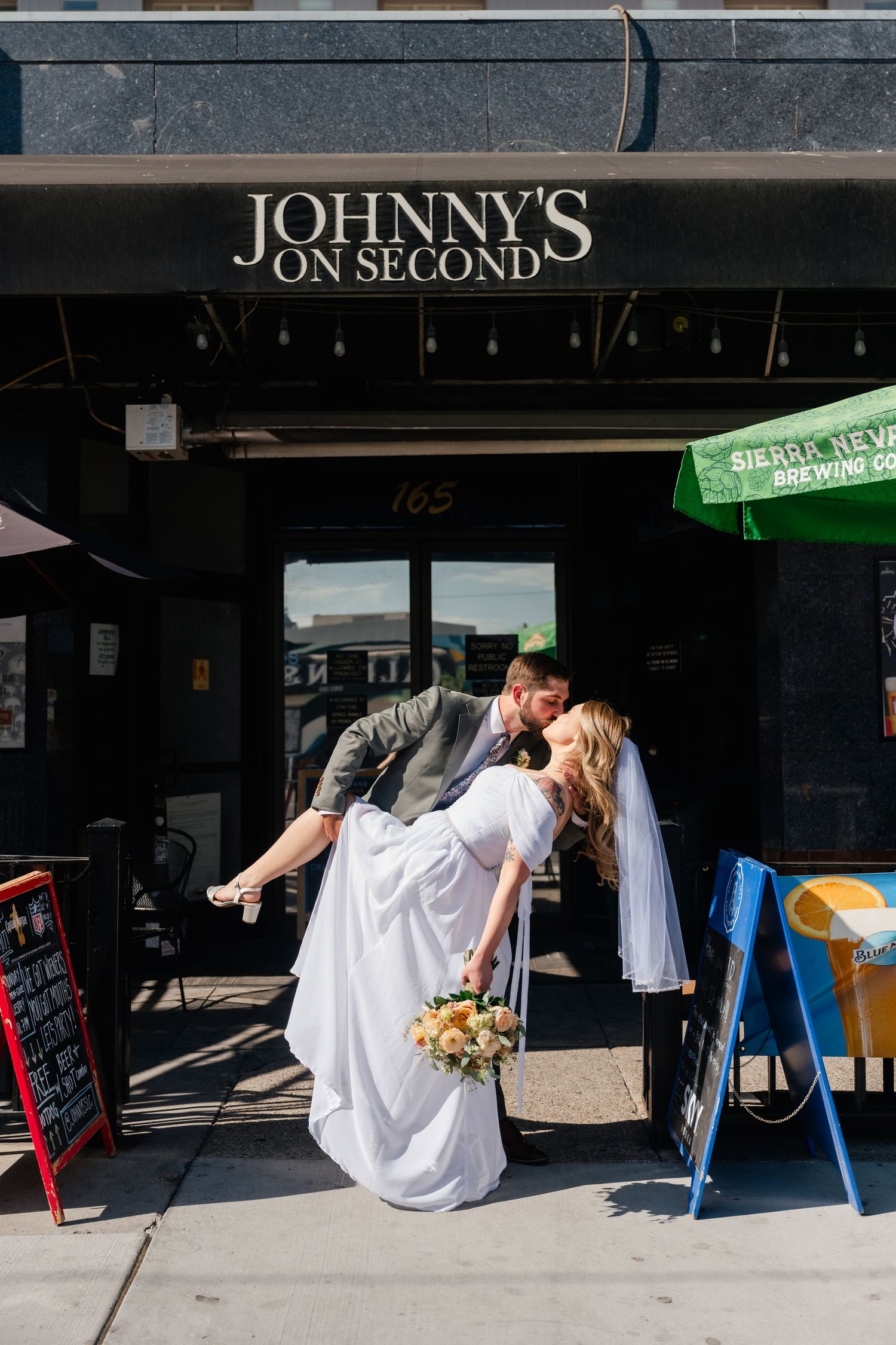 A romantic dip kiss outside Johnny's on Second with the bride holding a bouquet.
