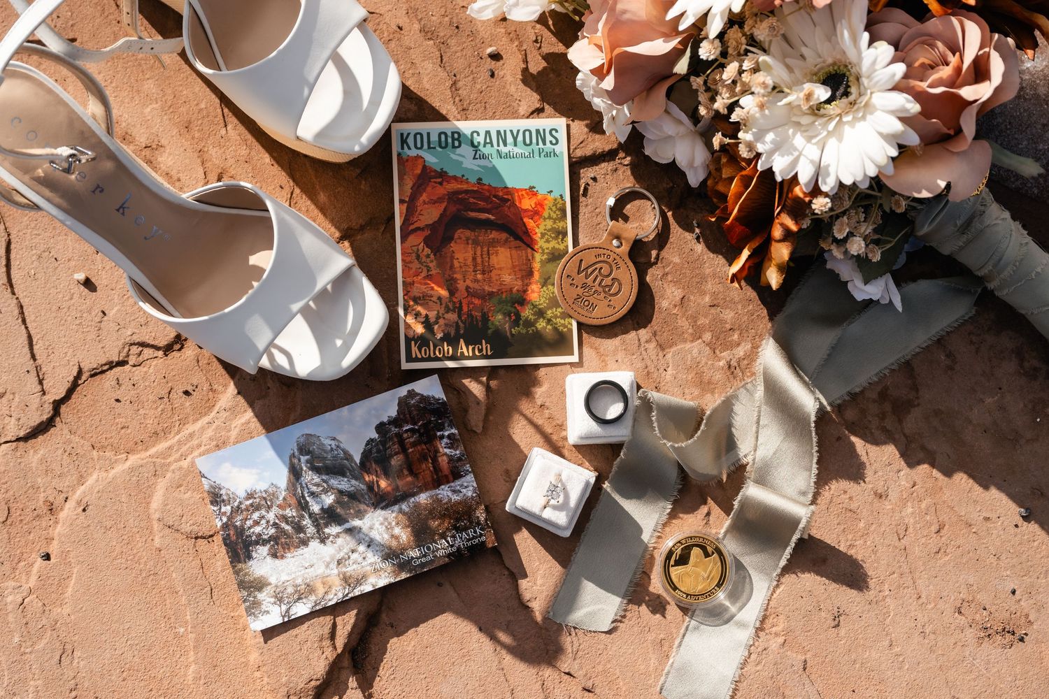 Wedding details including rings, flowers, and decorative elements arranged on red desert rock.