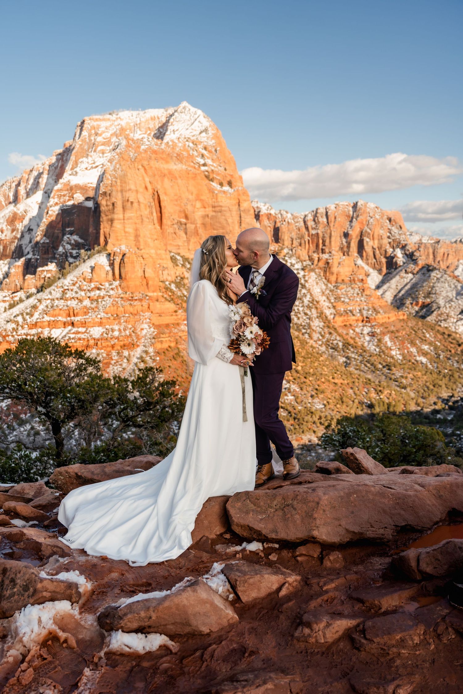 Wedding couple poses on red rock formations with stunning canyon views and blue skies in the background.