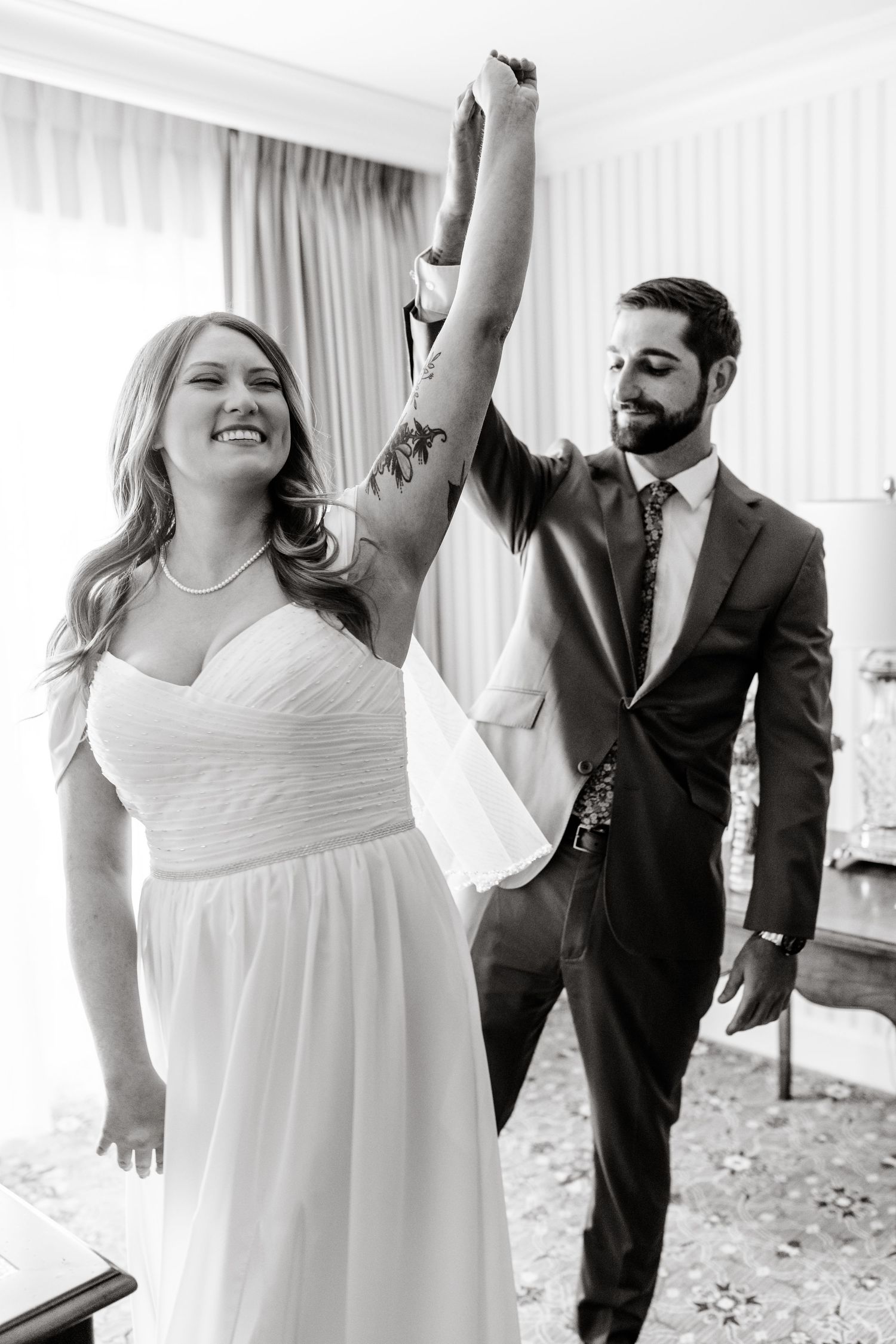 Joyful dancing sequence in white dress and dark suit against bright window backdrop.