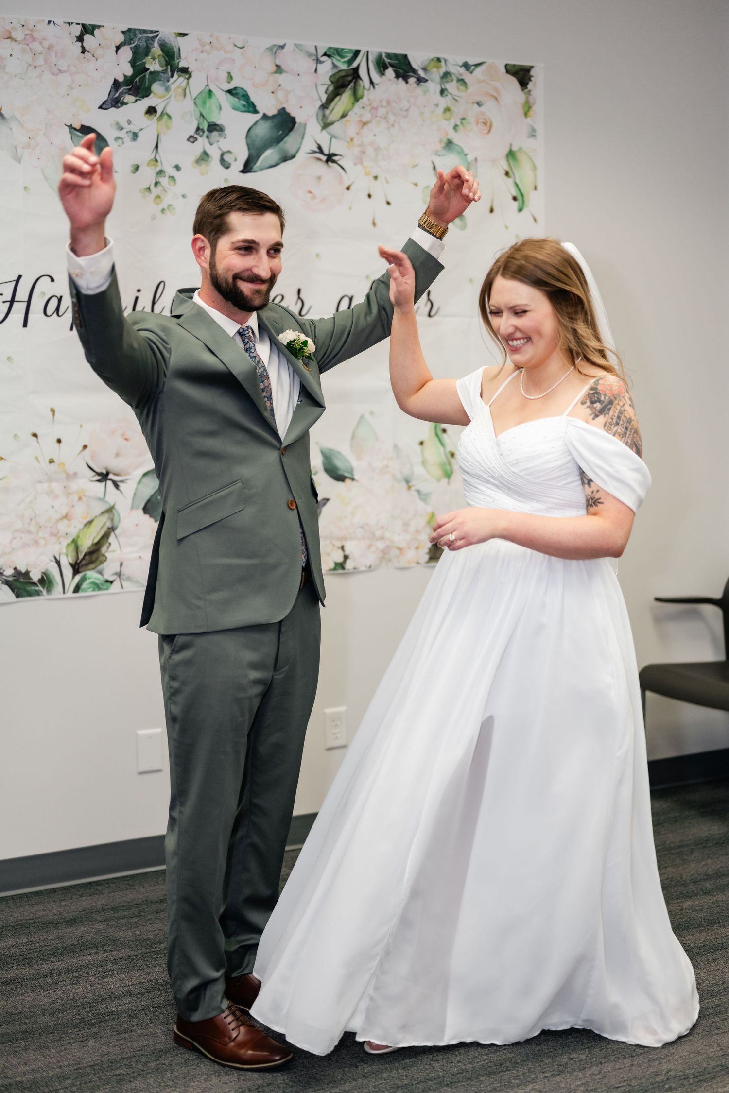 A joyful wedding couple dancing and celebrating in a room decorated with floral wall art.