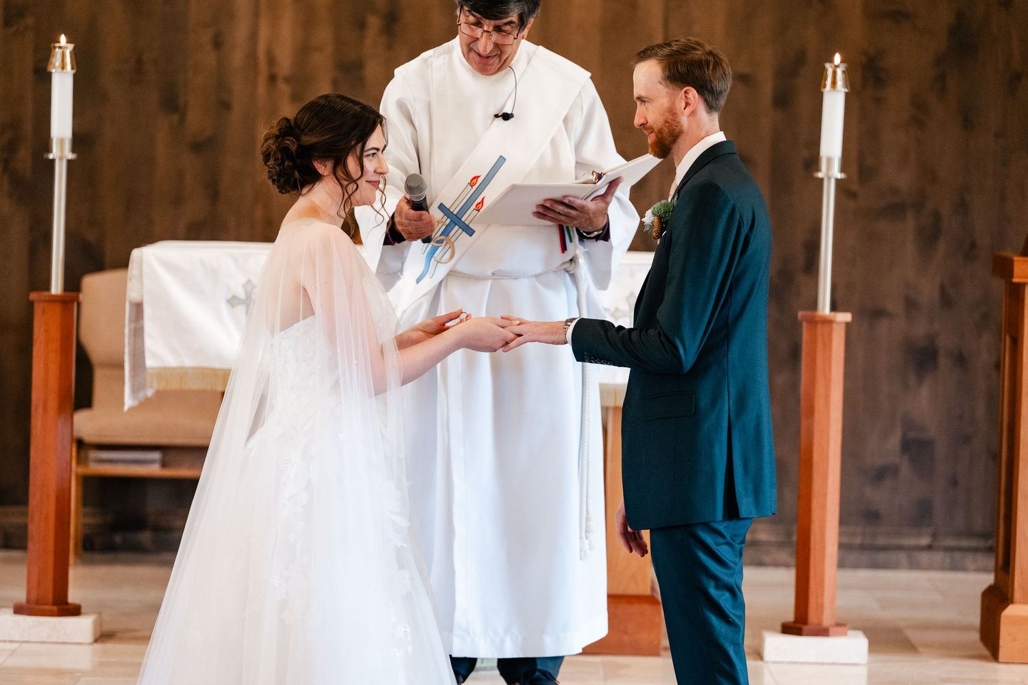 Wedding ceremony taking place at wooden altar with white candles and rustic decor.