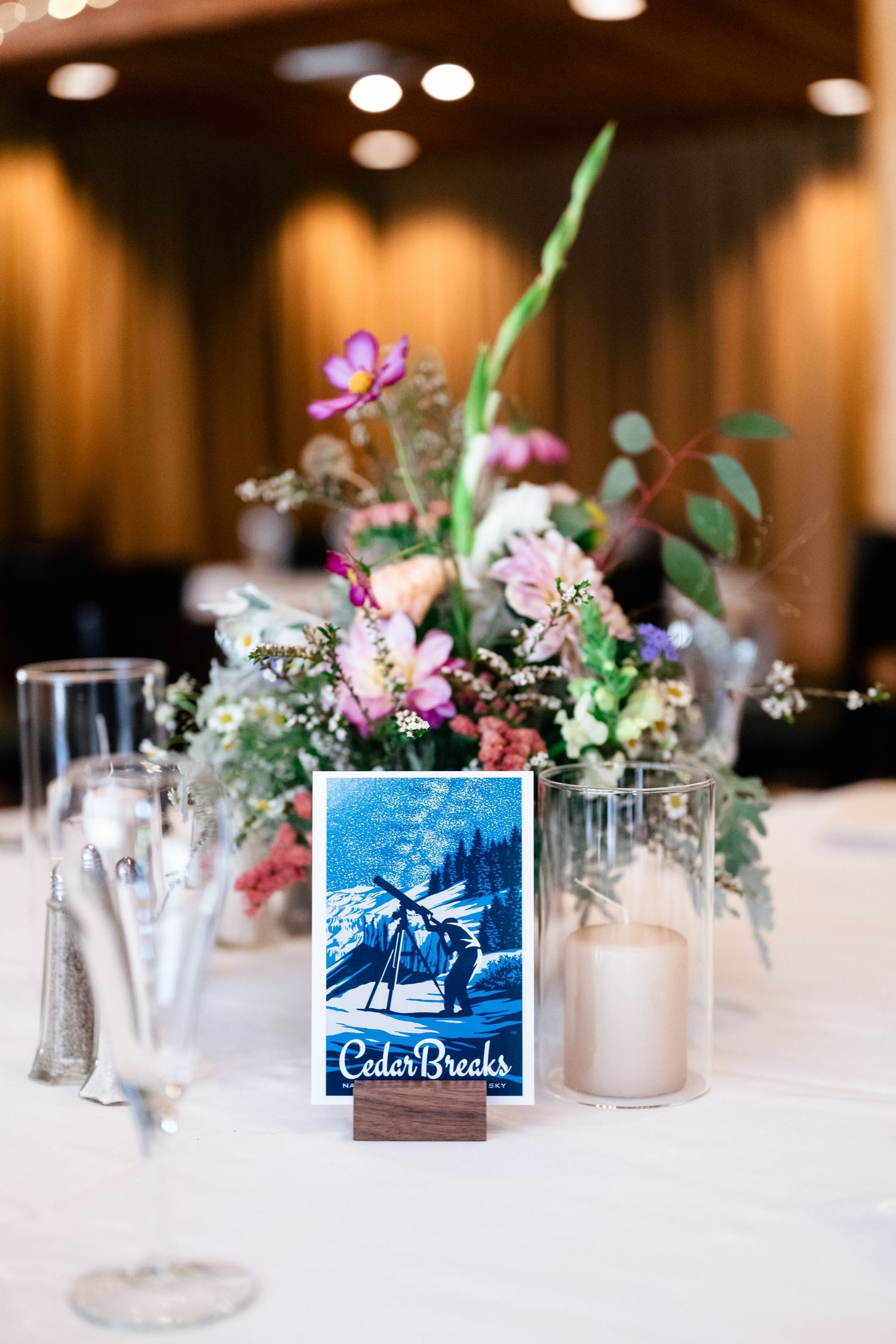 Elegant wedding table centerpiece with pink and purple flowers next to a framed Cedar Breaks destination card and glassware.
