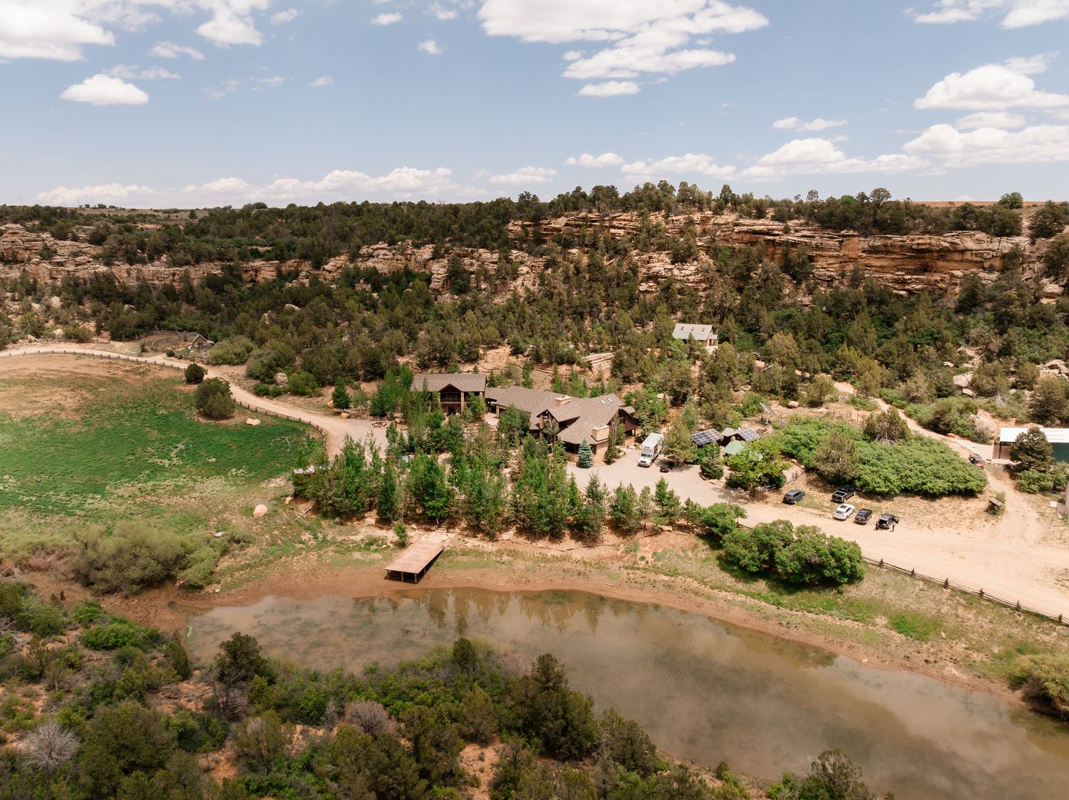 Aerial view of a scenic ranch property with a pond nestled among rolling hills and desert landscape.