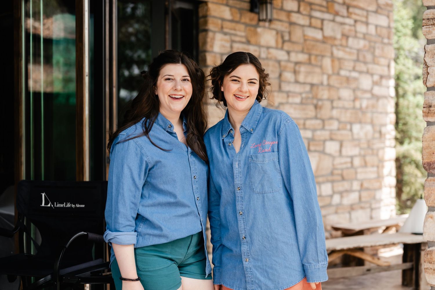 Two people in matching blue outfits smiling together against brick wall.