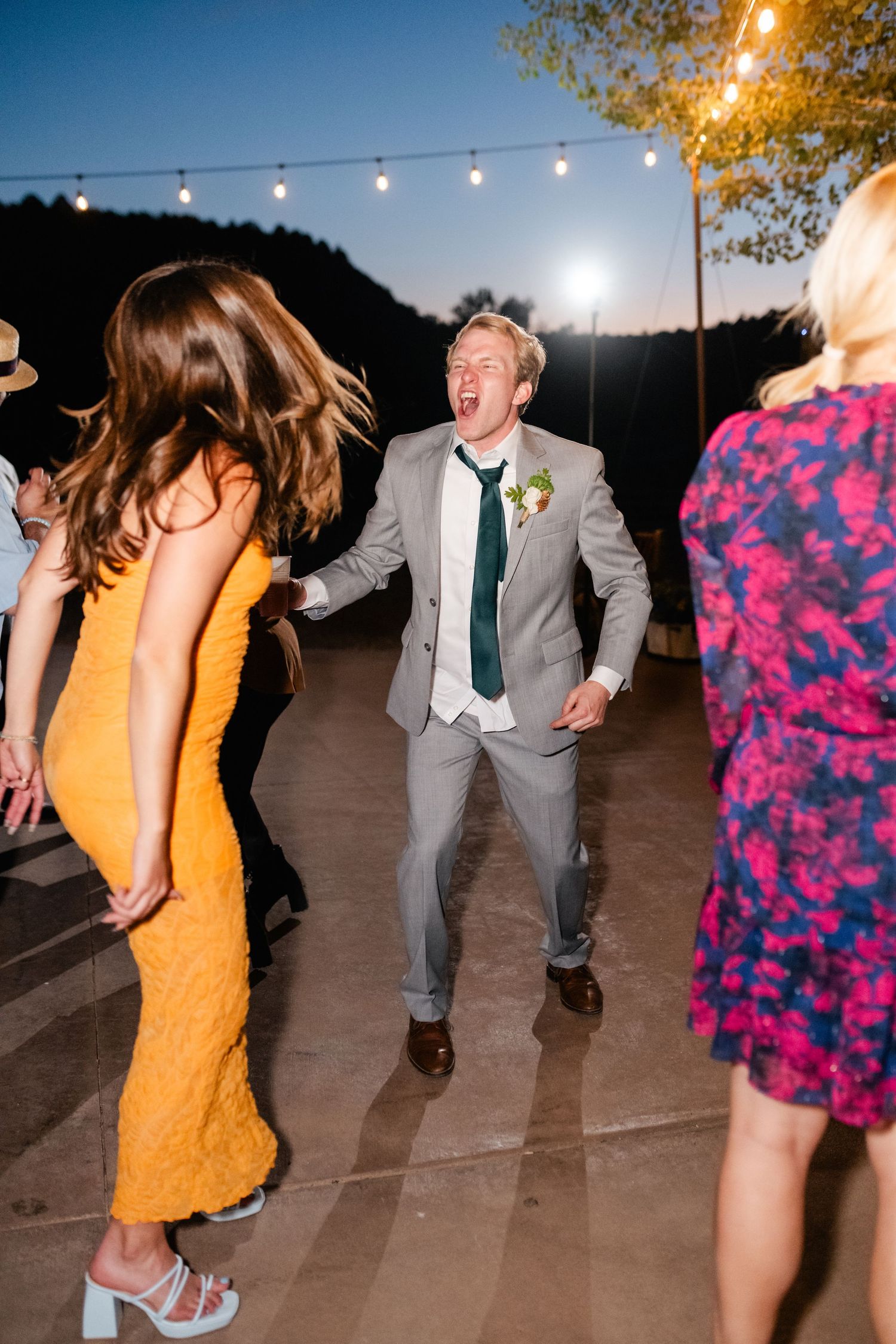 Wedding guests dance joyfully under string lights at outdoor evening reception.