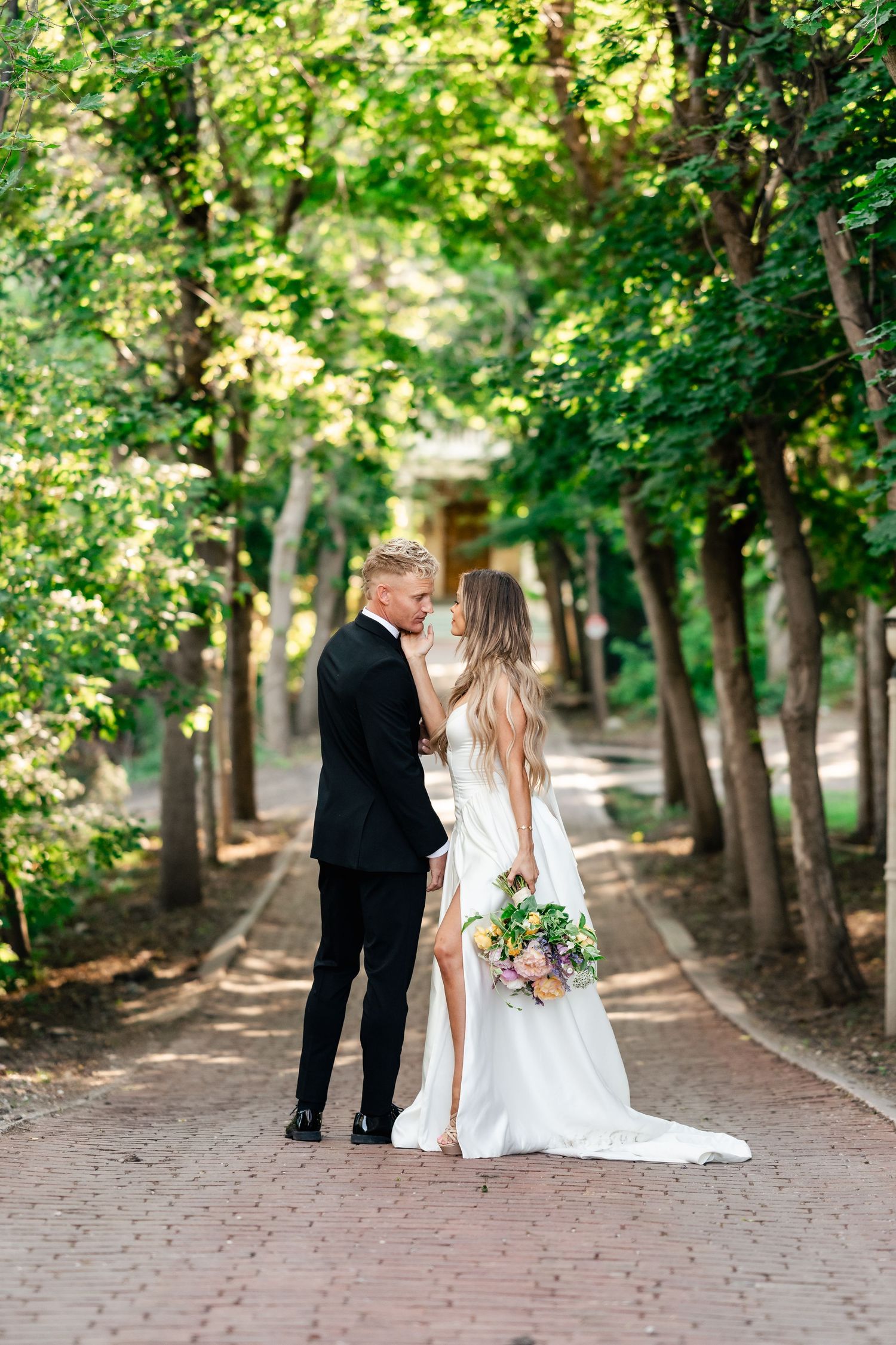 A romantic garden wedding photo series featuring a couple in formal attire walking along a tree-lined brick pathway.