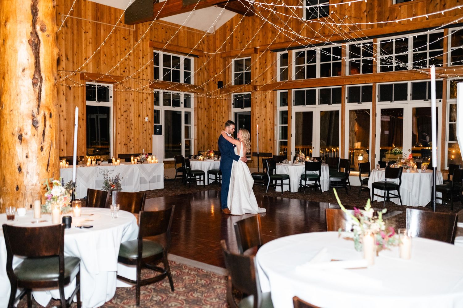 A spacious rustic wooden wedding venue with tall windows and white-clothed tables arranged for a reception. Utah Wedding Photographer.