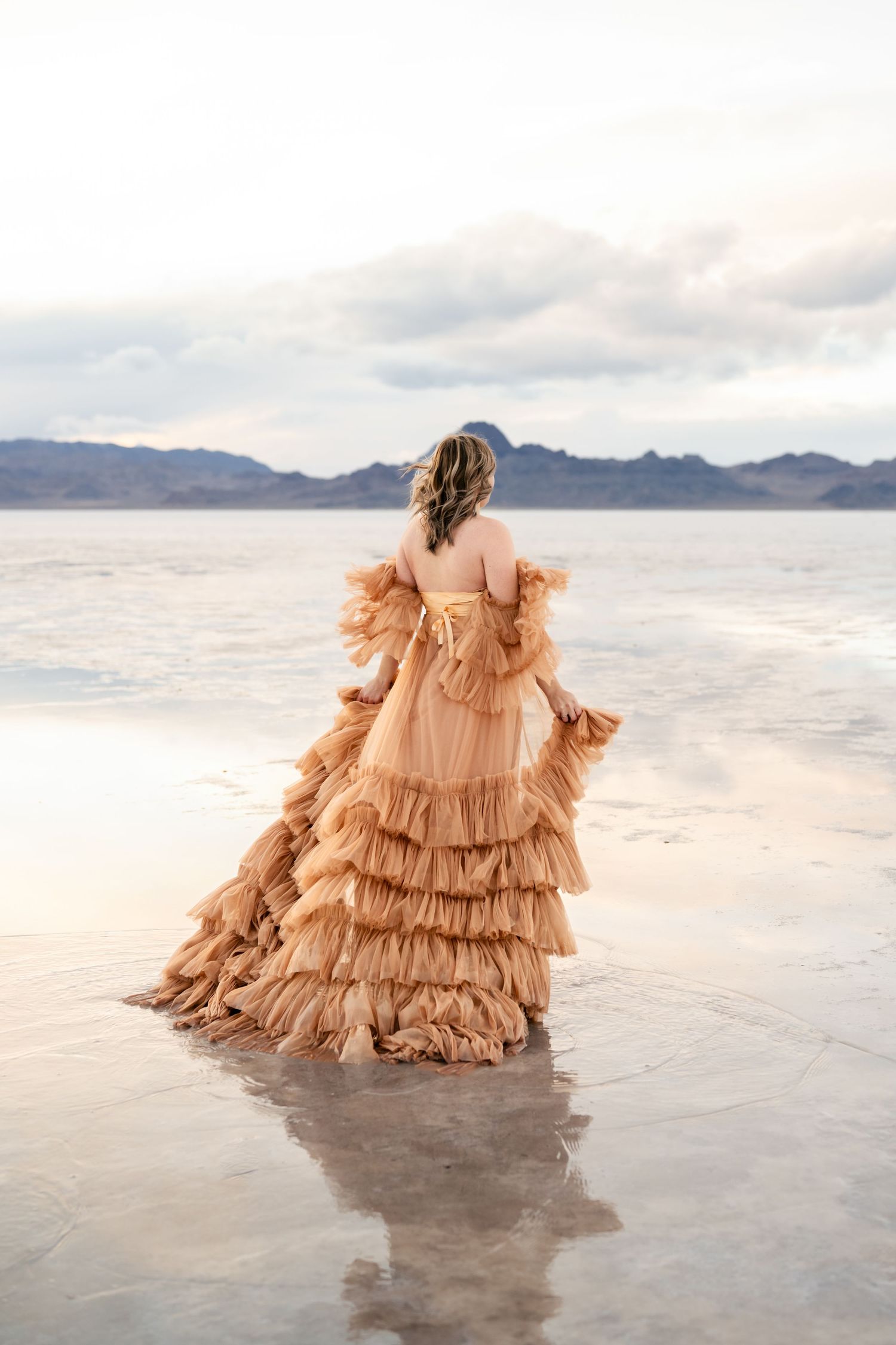 A couple poses together against the surreal backdrop of the flooded Salt Flats during golden hour.