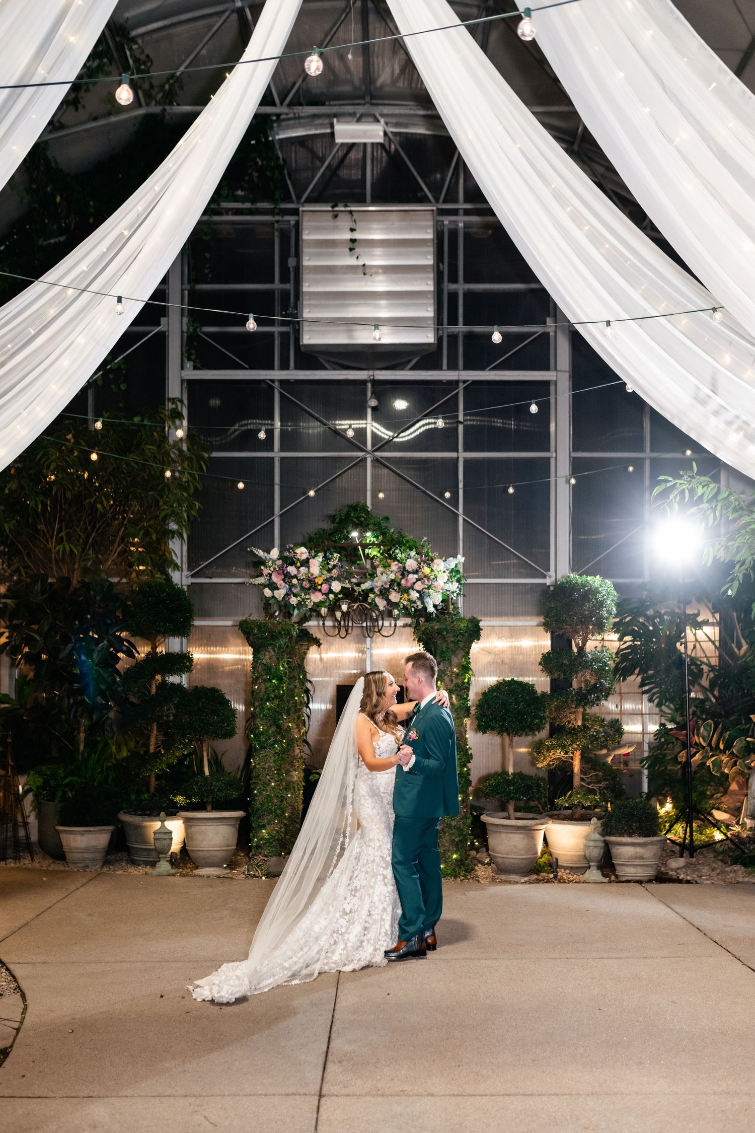 A romantic wedding scene with white draping and string lights decorating an elegant indoor venue.
