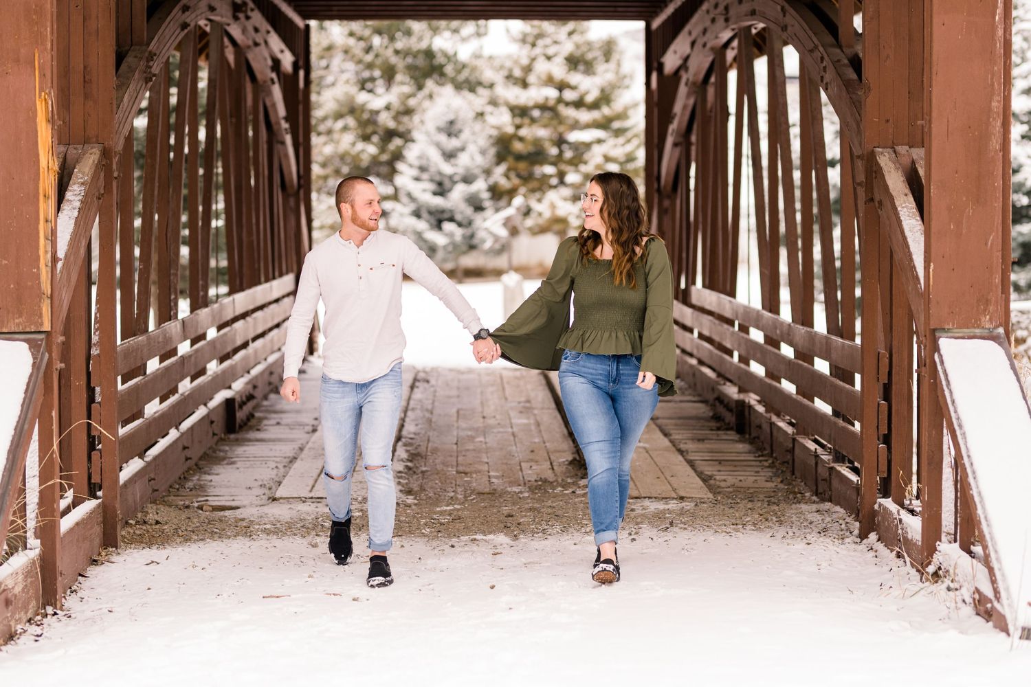 A couple runs playfully through a covered wooden bridge during winter.