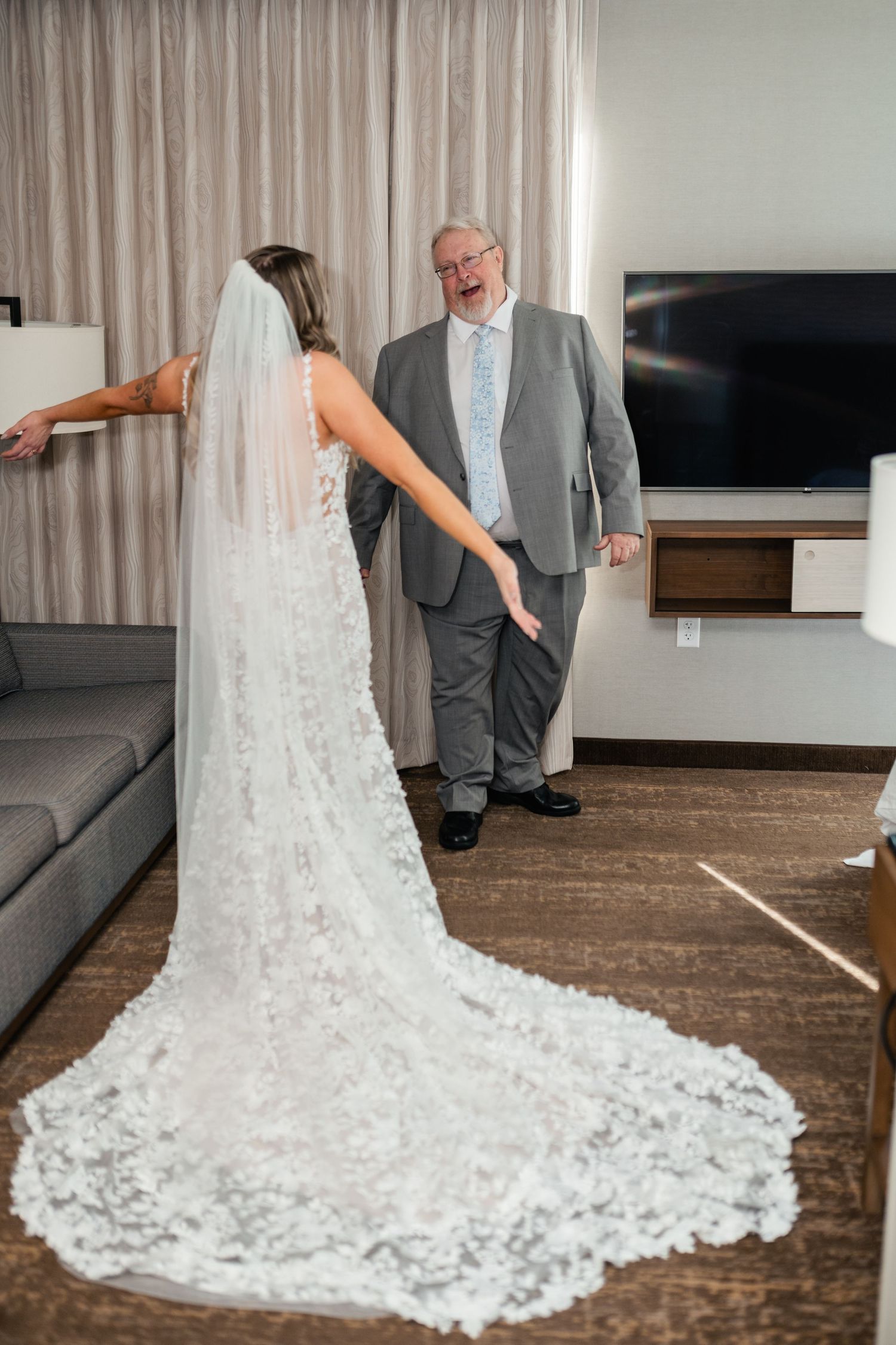 A tender first look moment between a bride in a stunning lace train wedding dress and a gentleman in a grey suit.