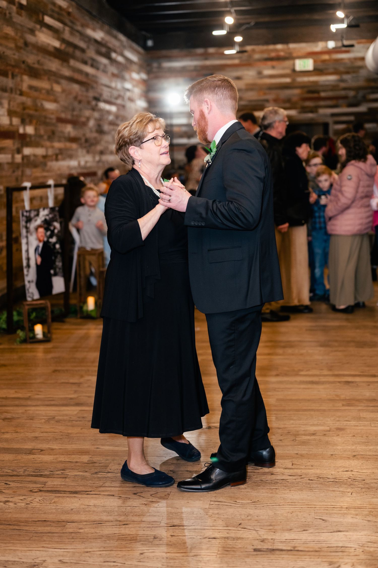 Couple shares emotional dance moment on wooden floor at rustic indoor reception venue.