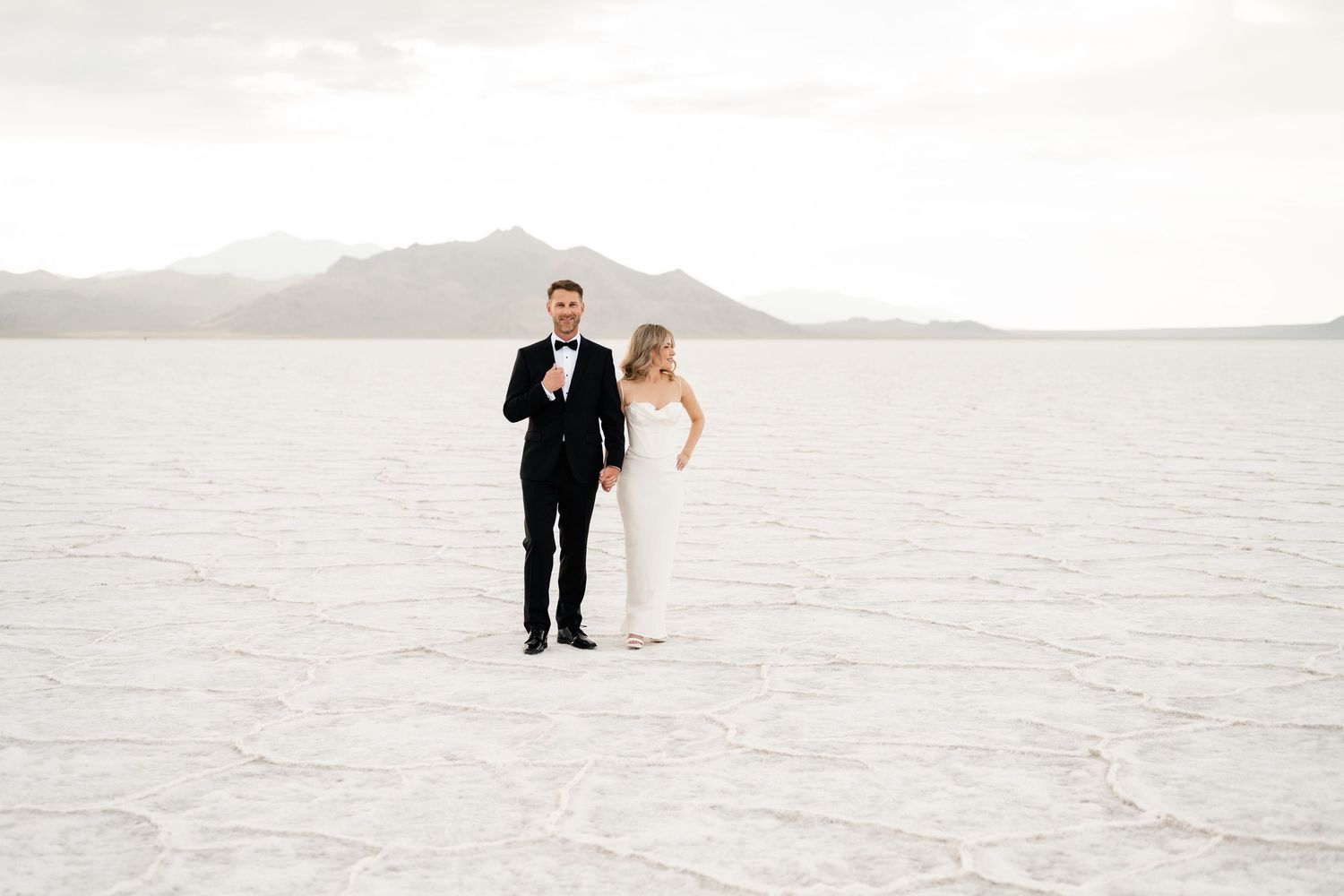 Salt Flats Elopement Photographer. Two people walk together across a vast white salt flat landscape during golden hour.