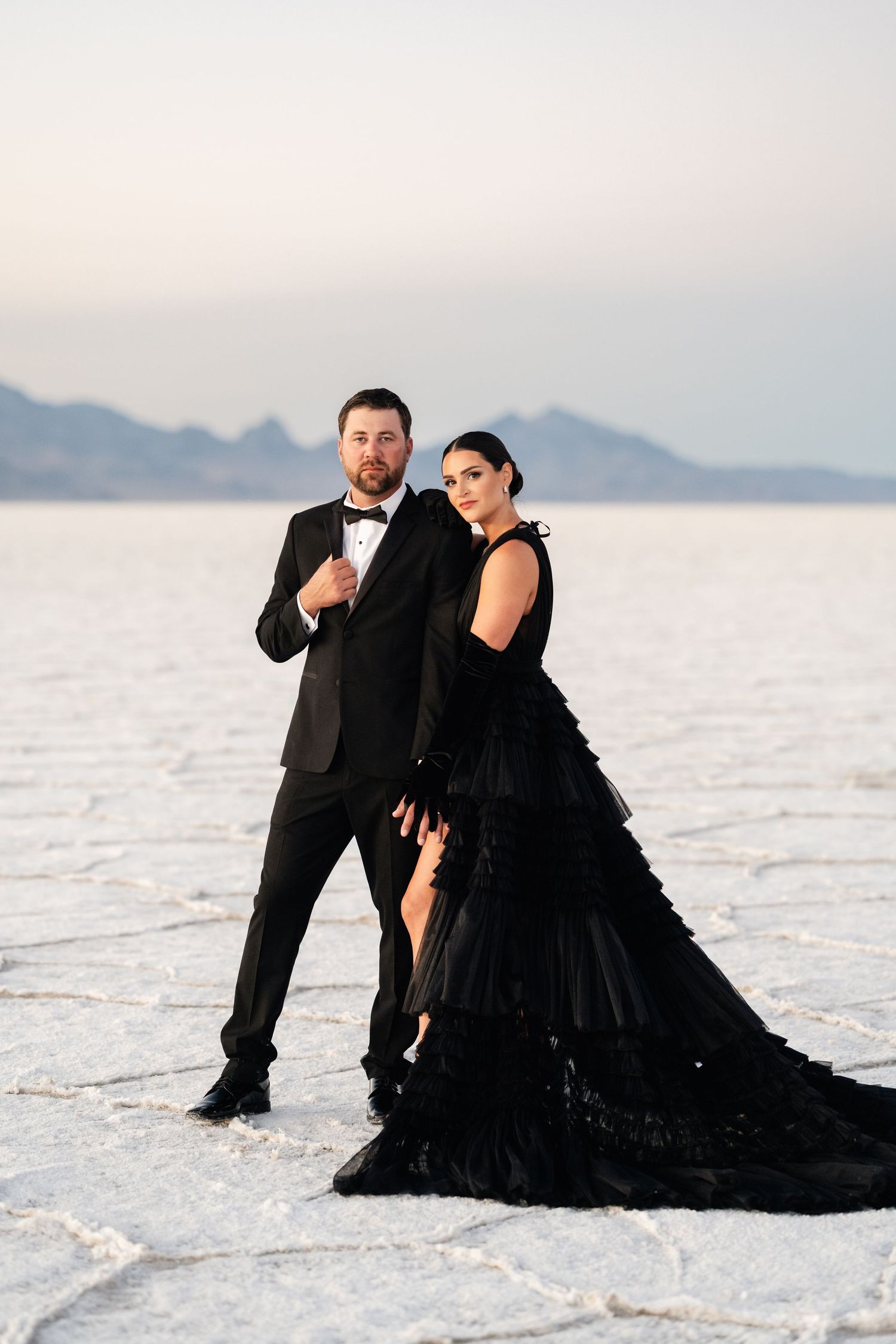 Utah Salt Flats Photographer. A couple in formal attire poses together on white salt flats with mountains in the background.