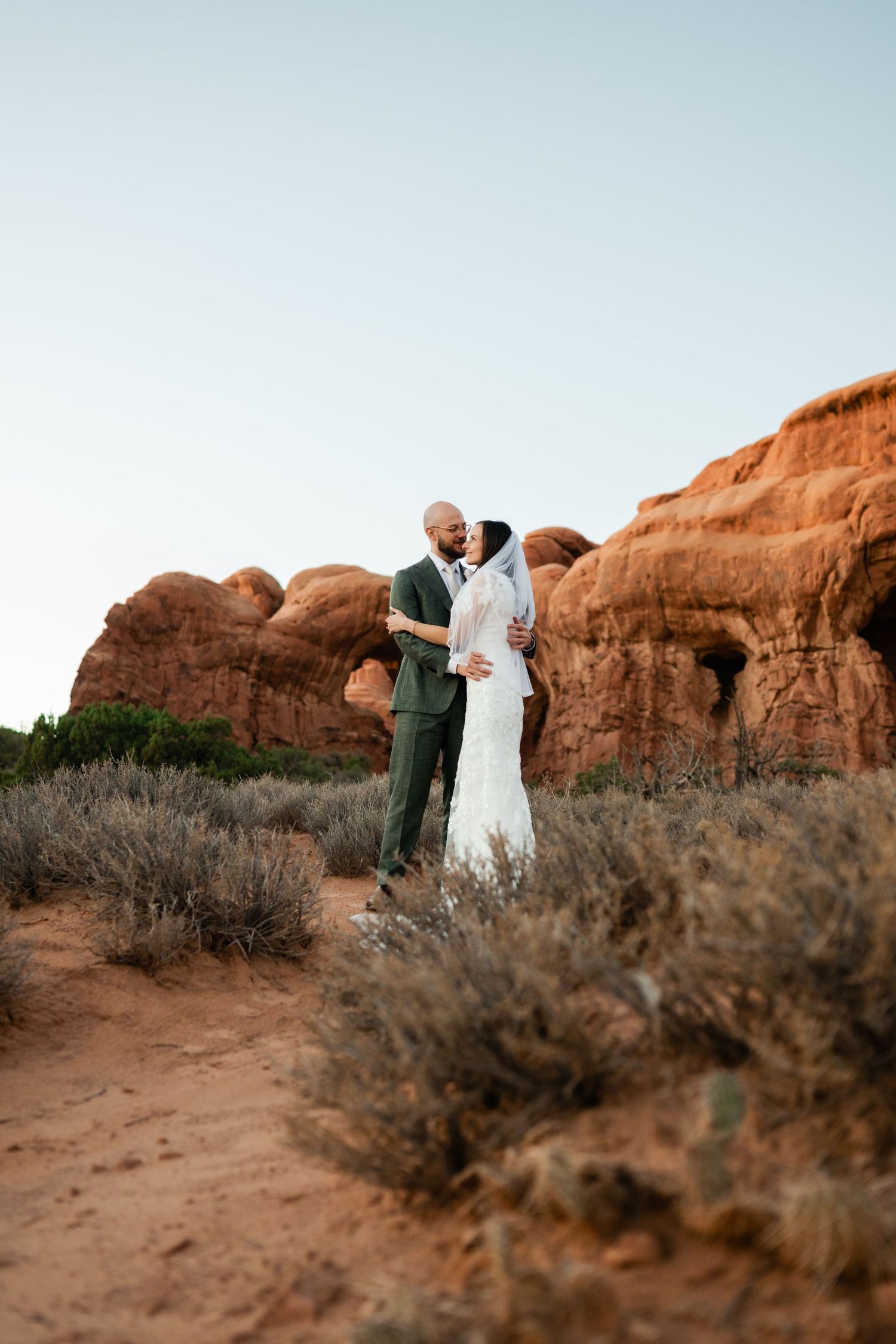 A couple shares an intimate moment against the backdrop of red rock formations in Arches National Park at sunset.
