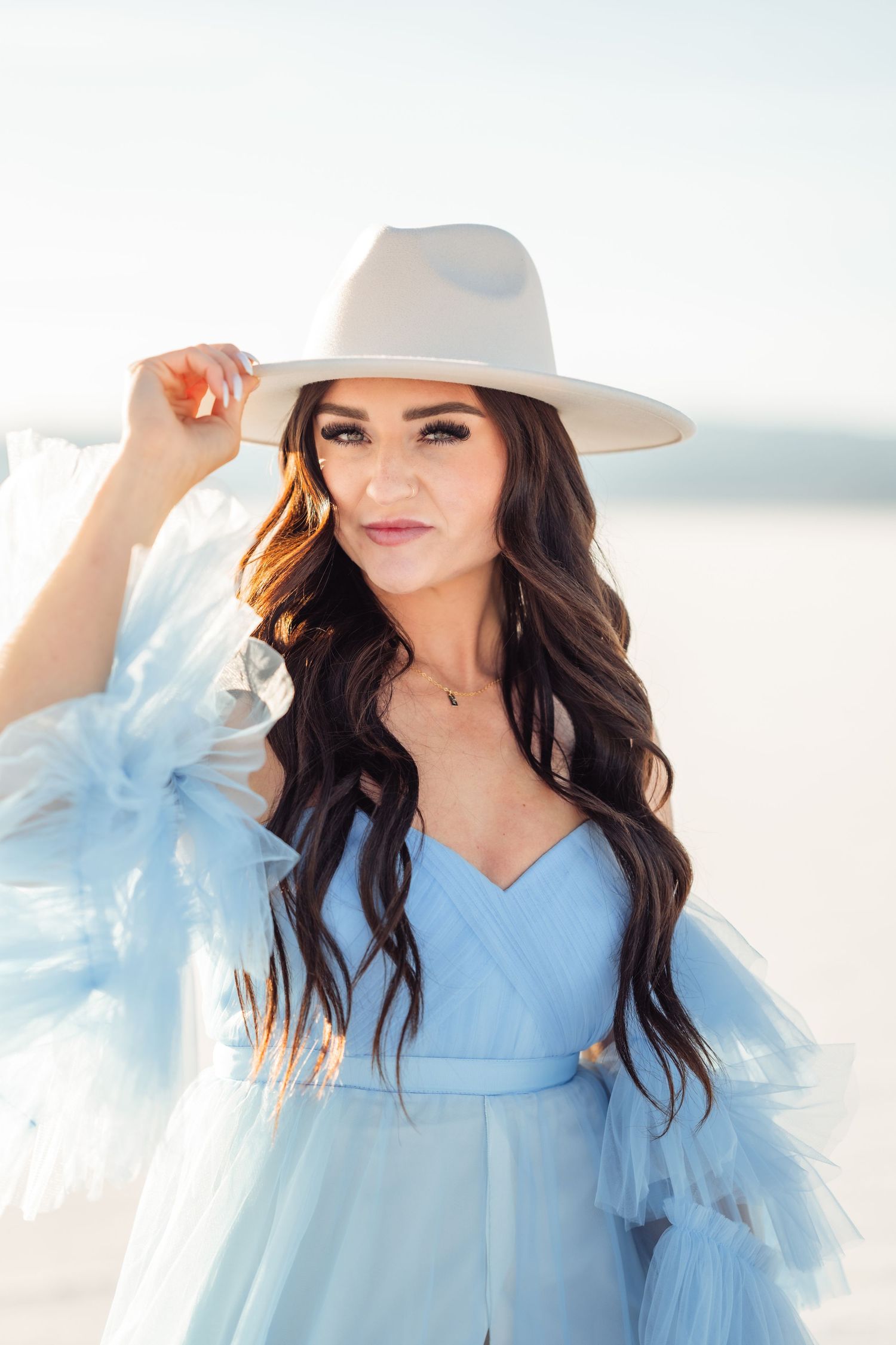 Utah Salt Flats Photographer. Ethereal portrait of a woman in a light blue tulle dress and wide brim hat against a bright outdoor backdrop.
