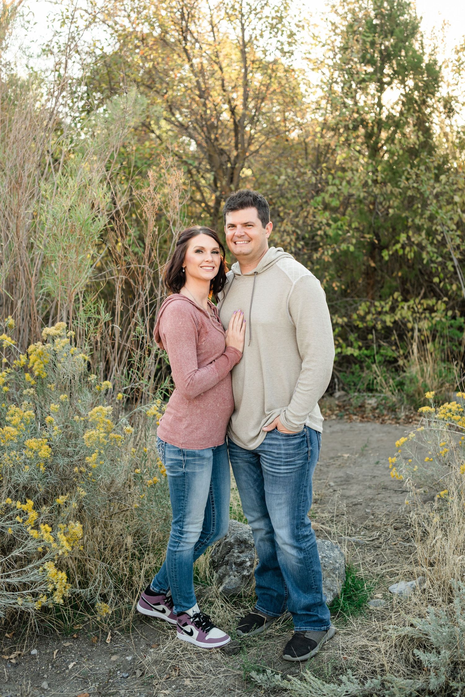 A couple in casual attire shares tender moments together in a natural outdoor setting with yellow wildflowers.