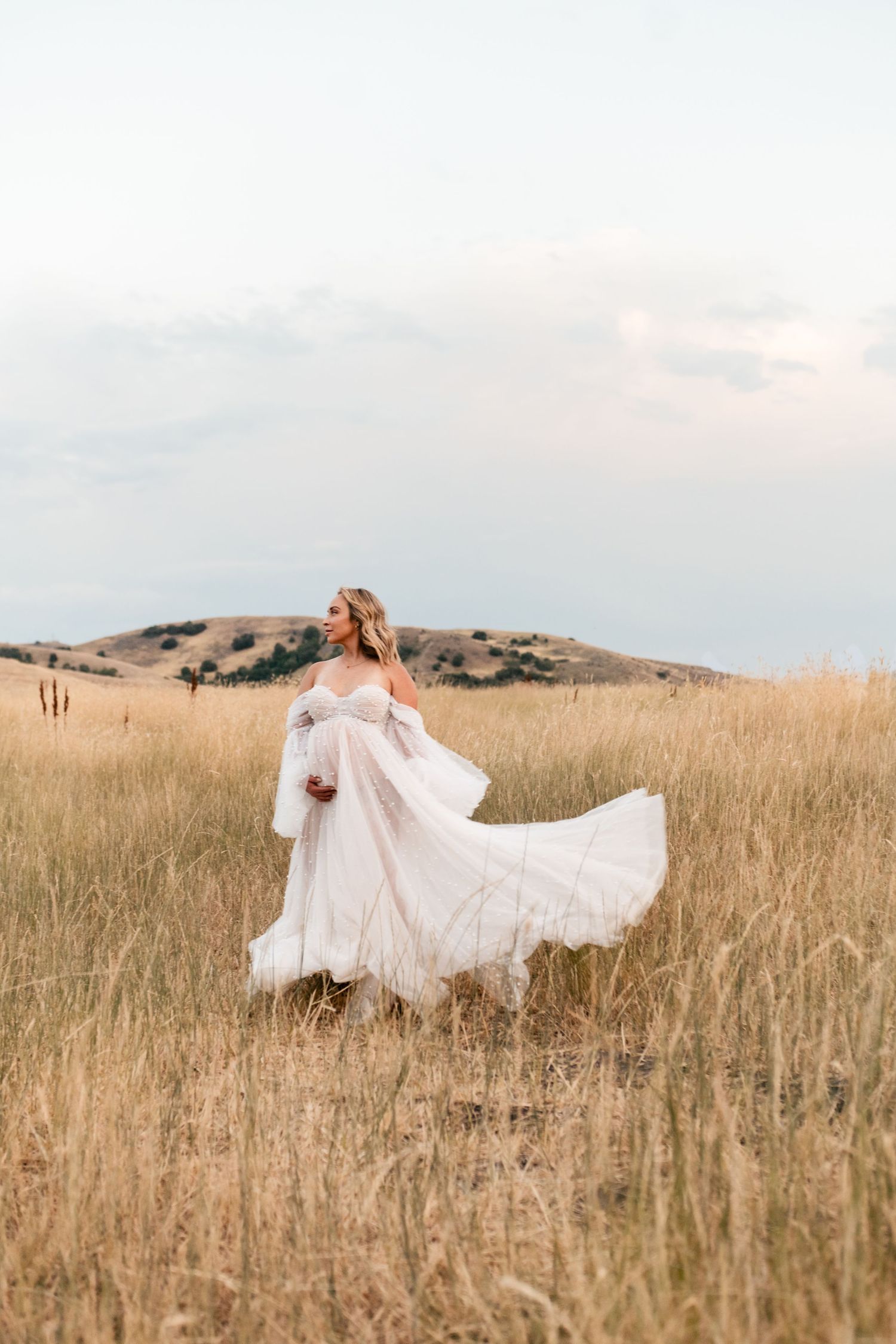 A flowing white wedding dress billows in the wind as a figure stands in a golden field at sunset.