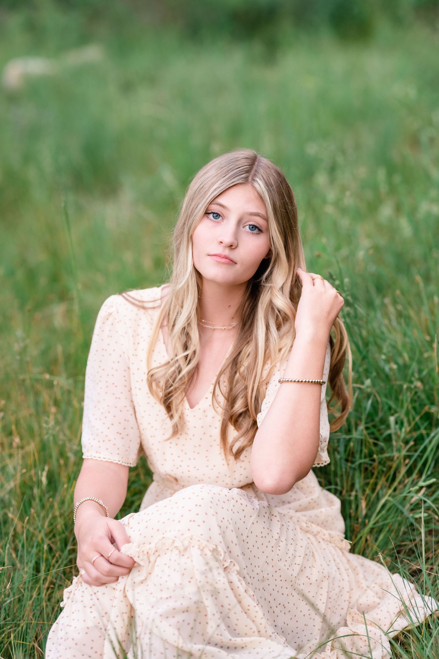 A person in a polka dot dress lies in a green meadow surrounded by tall grass on a summer day.
