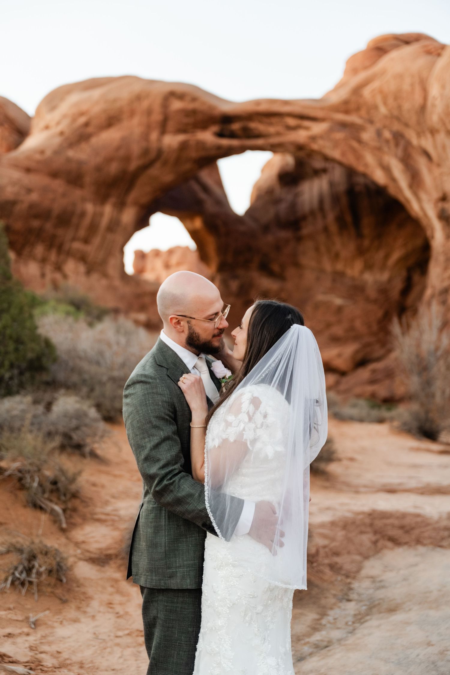 A couple shares an intimate moment among the red rock formations of Arches National Park during their desert wedding.