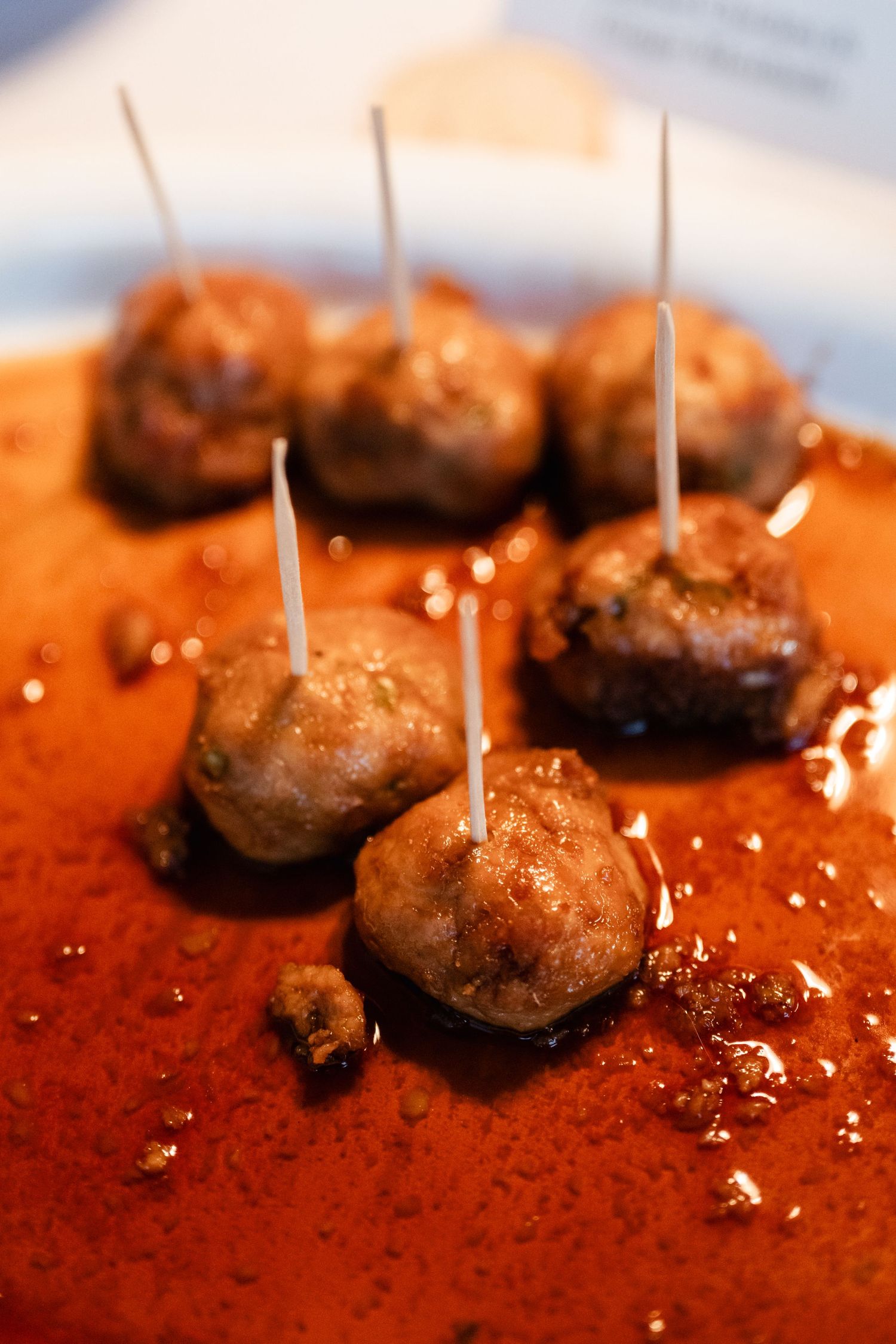Close-up of glazed meatballs with toothpicks on a rich orange-colored sauce.