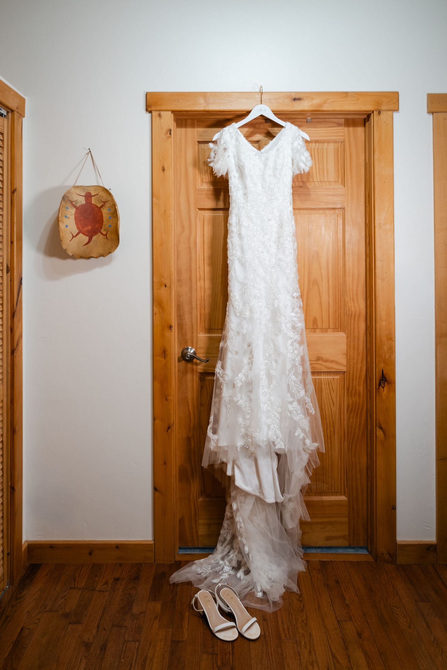 White lace wedding dress and shoes hanging on wooden doors in a rustic interior setting.