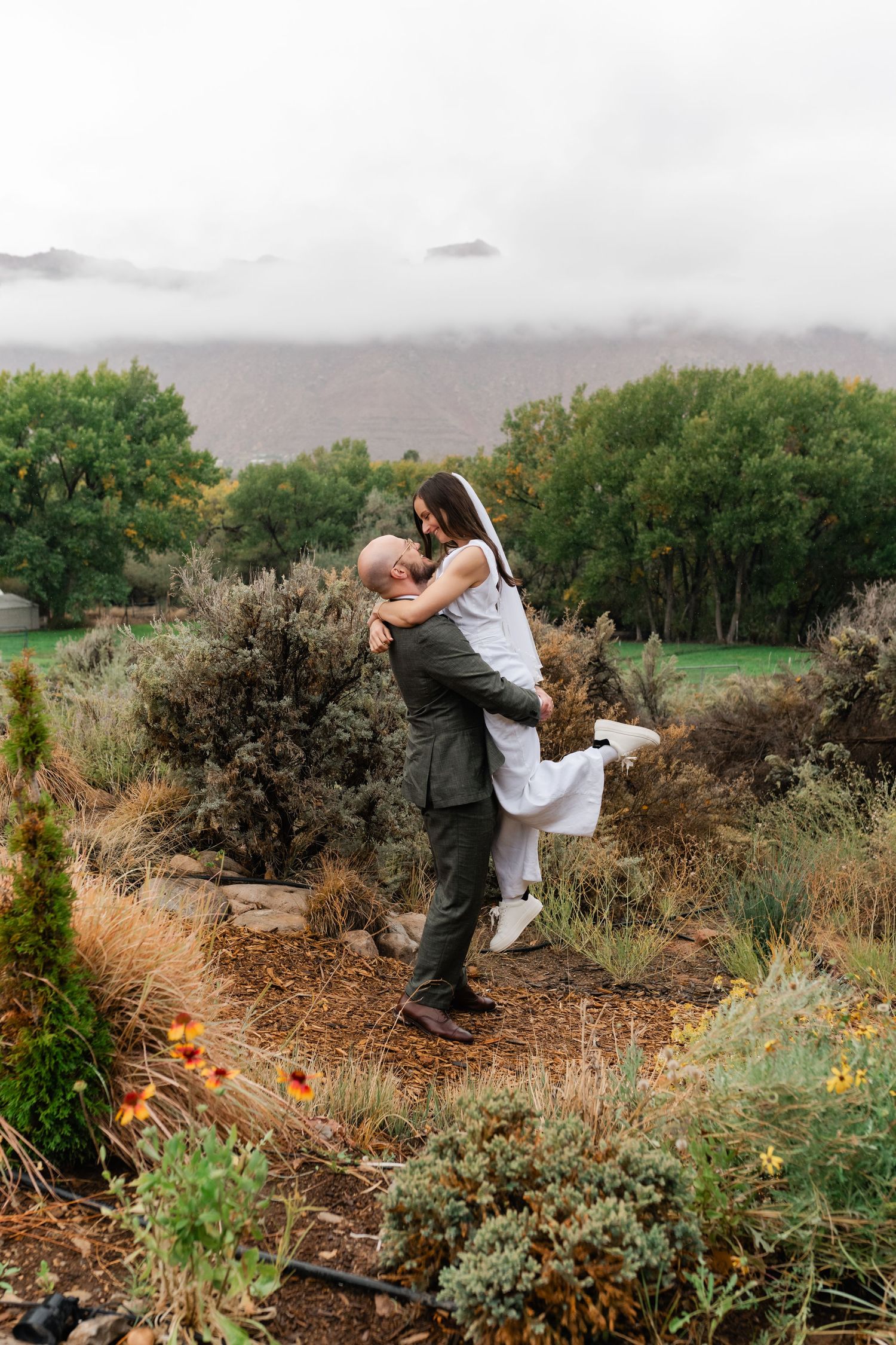 Newlyweds embrace among desert brush and wildflowers on their wedding day.