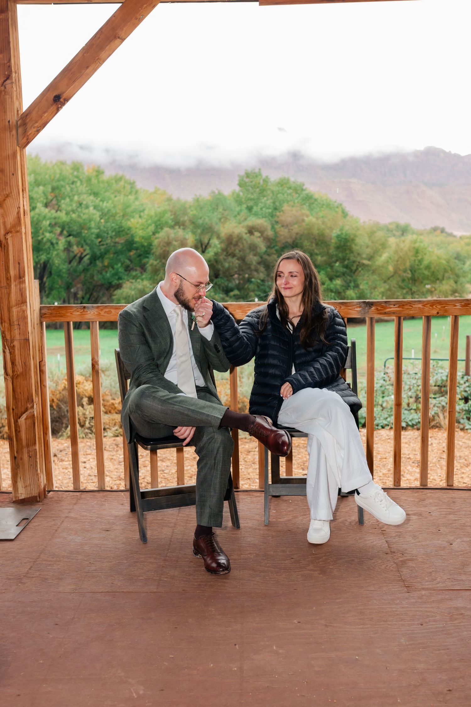 A couple shares a tender moment on a rustic wooden deck overlooking a scenic mountain landscape.
