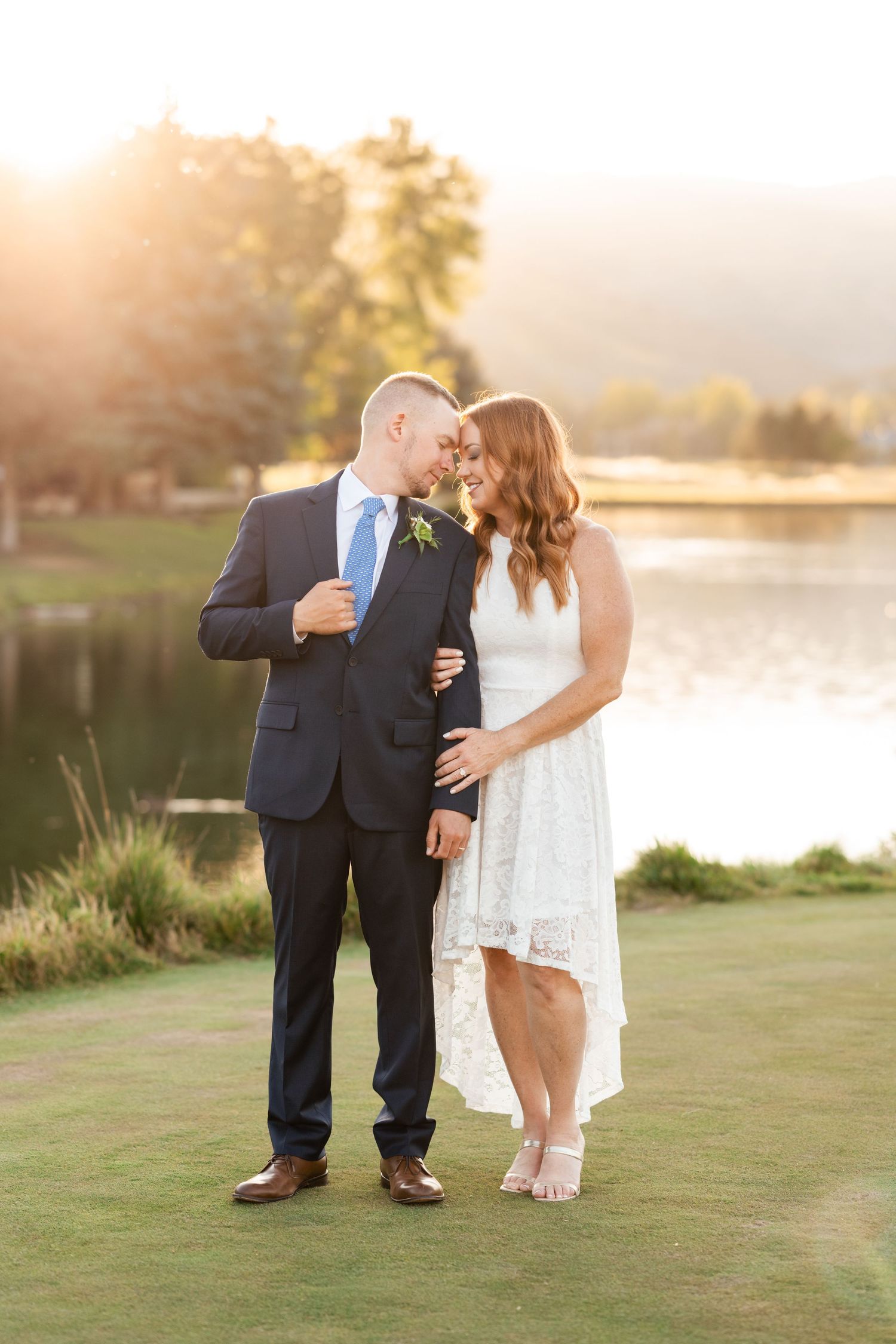 A romantic sunset wedding photo of a couple embracing on a golf course beside a serene lake.