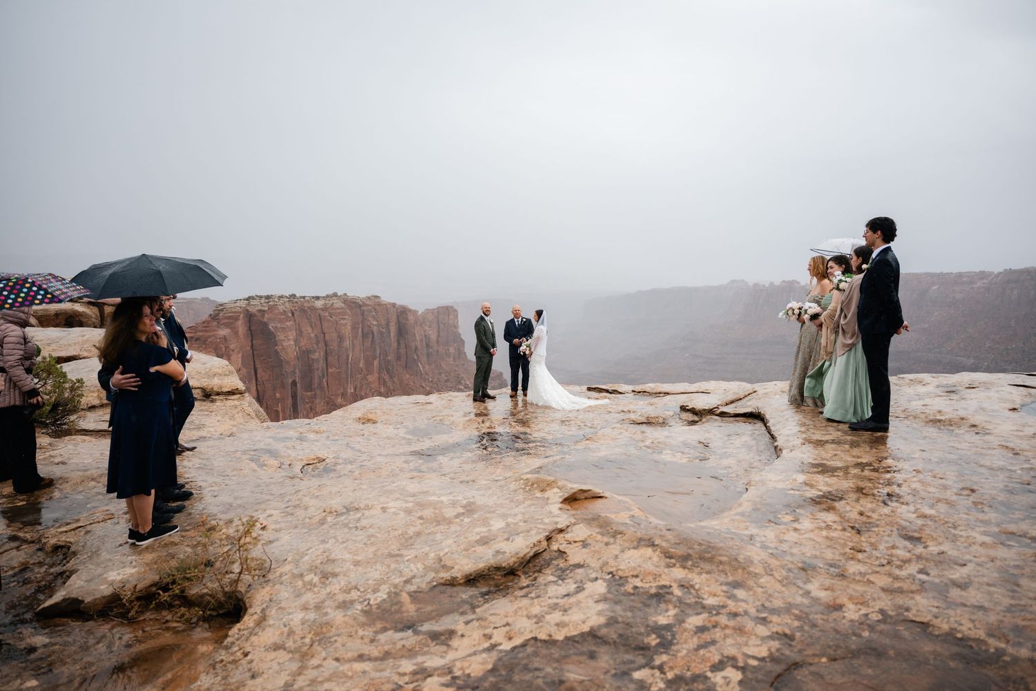 Wedding guests and couple gathered on rocky cliff edge with sweeping canyon views.