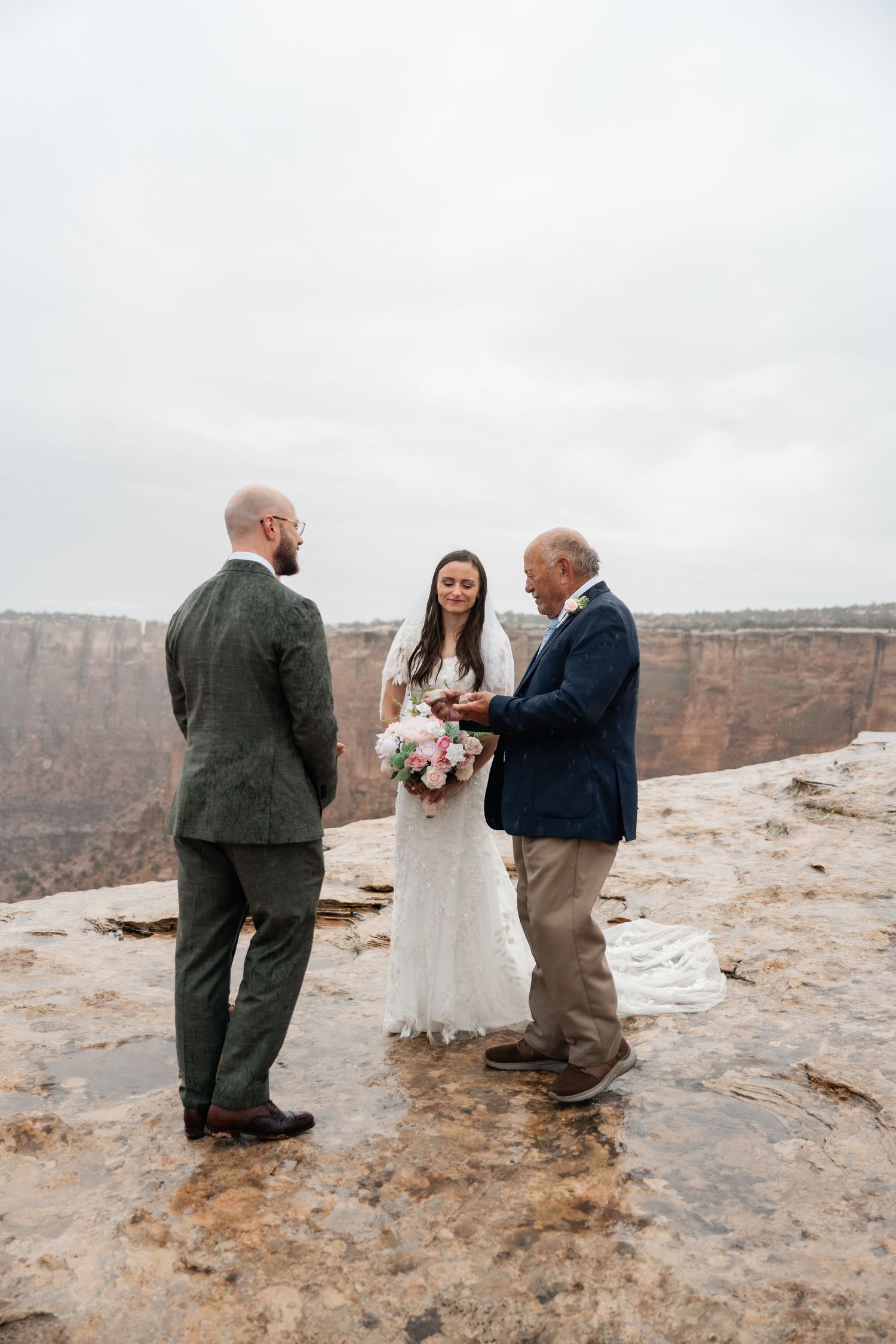 An intimate wedding ceremony takes place on the edge of a dramatic canyon overlook with stunning desert vistas in the background.