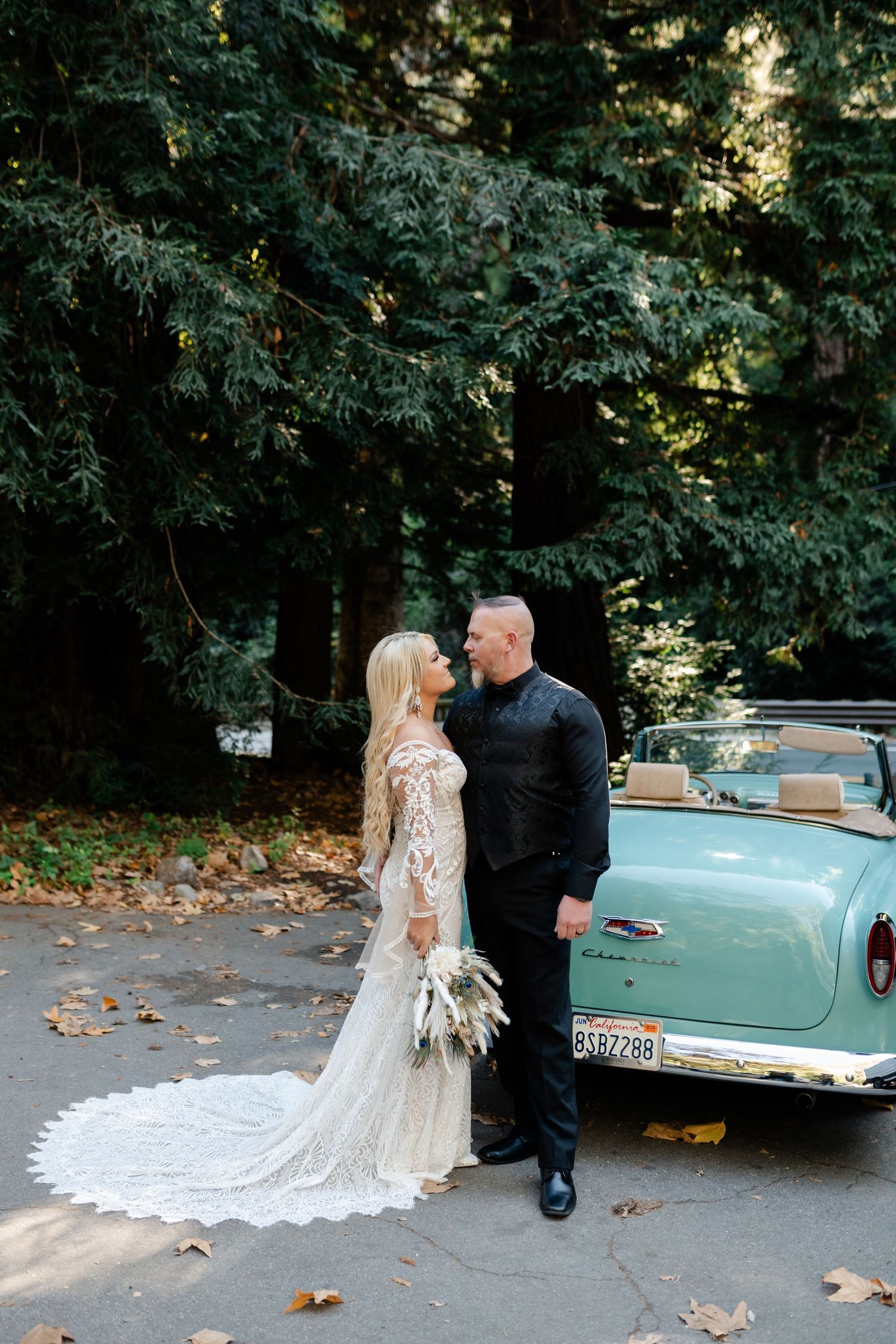 Vintage turquoise classic car parked among trees with wedding couple.