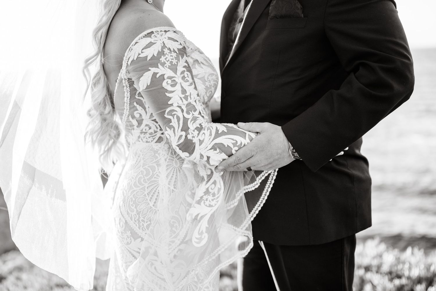 Close up black and white detail of intricate lace wedding dress pattern against a dark suit.