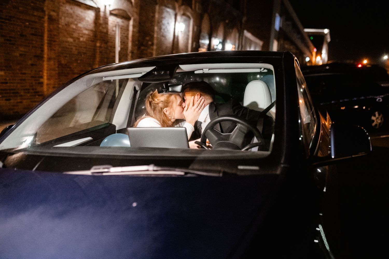 A nighttime scene of a car parked outside a brick building with illuminated windows.