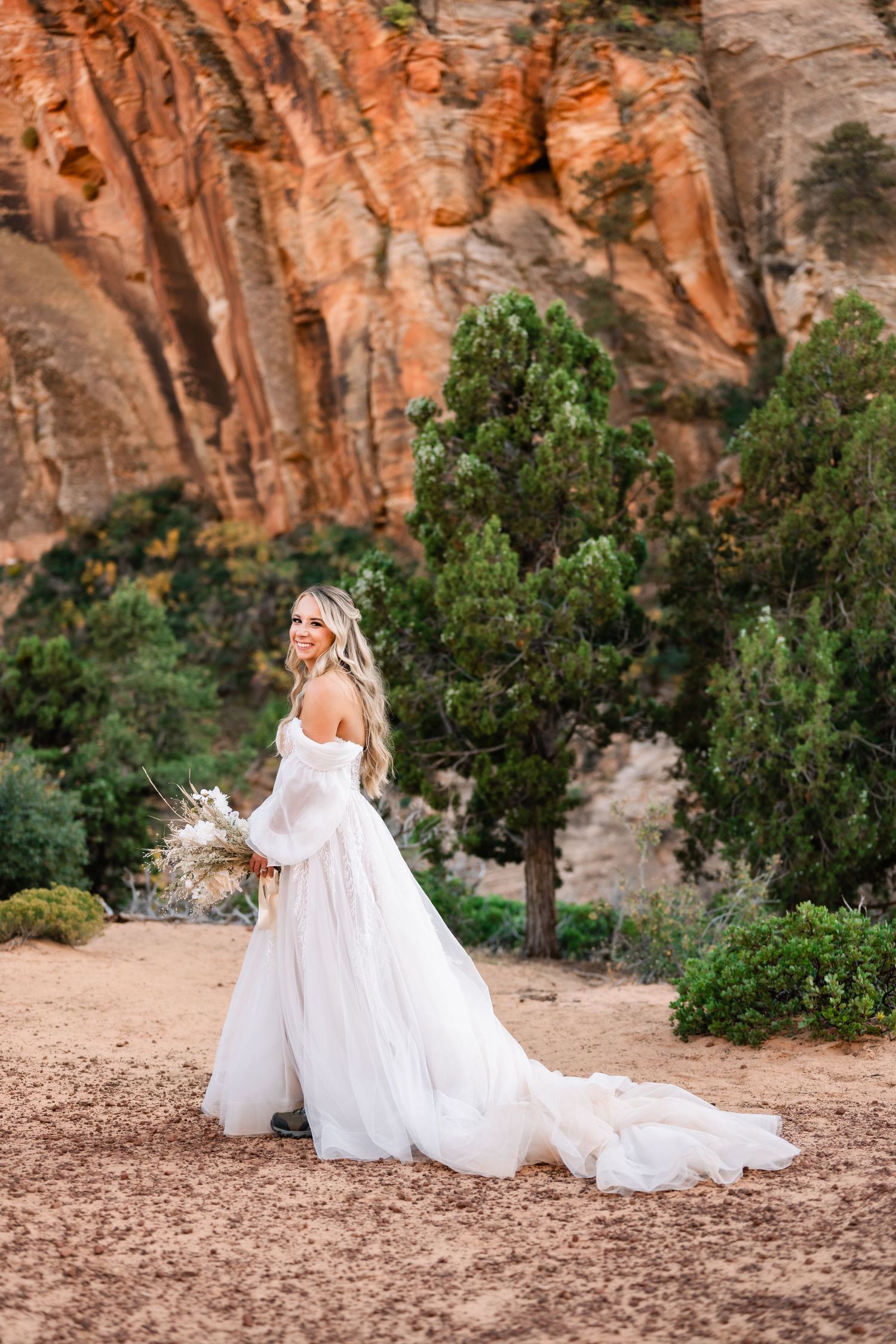 A flowing white wedding dress creates movement against red rock canyon landscape.