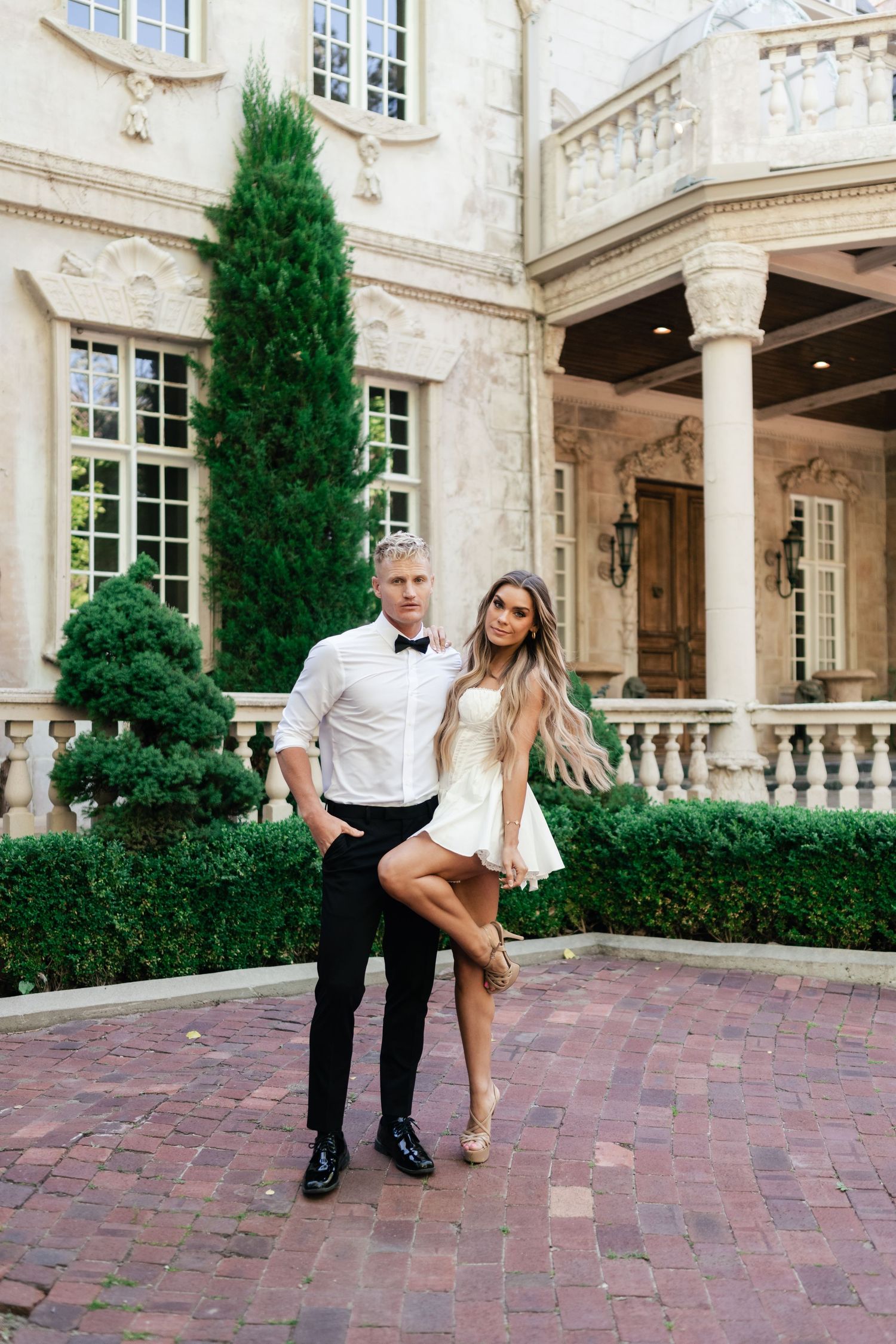 Wedding couple recreates iconic dance move outside elegant stone courtyard with pillars and cypress trees.