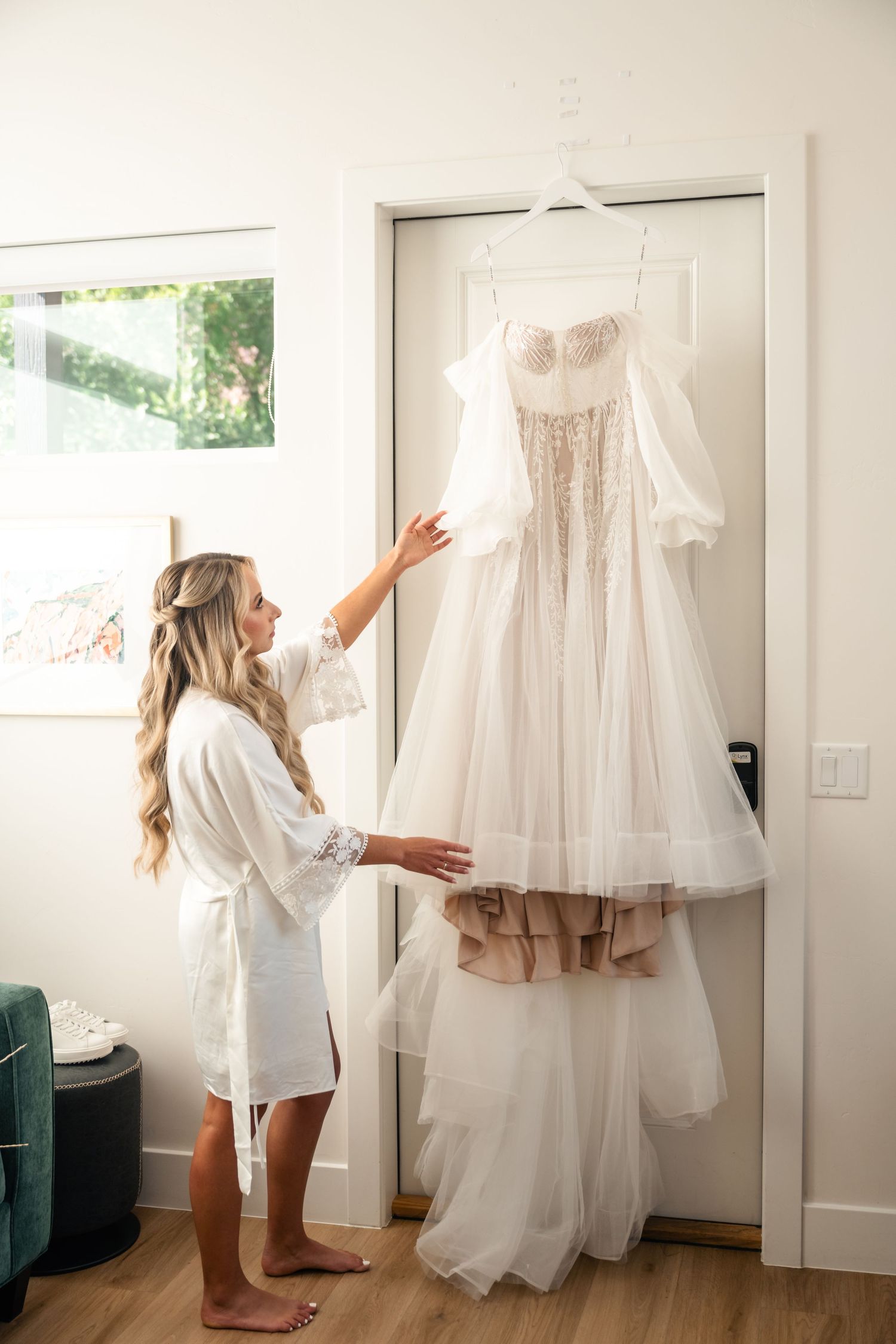 Wedding dress being admired in bright room with green velvet couch and hardwood floors.