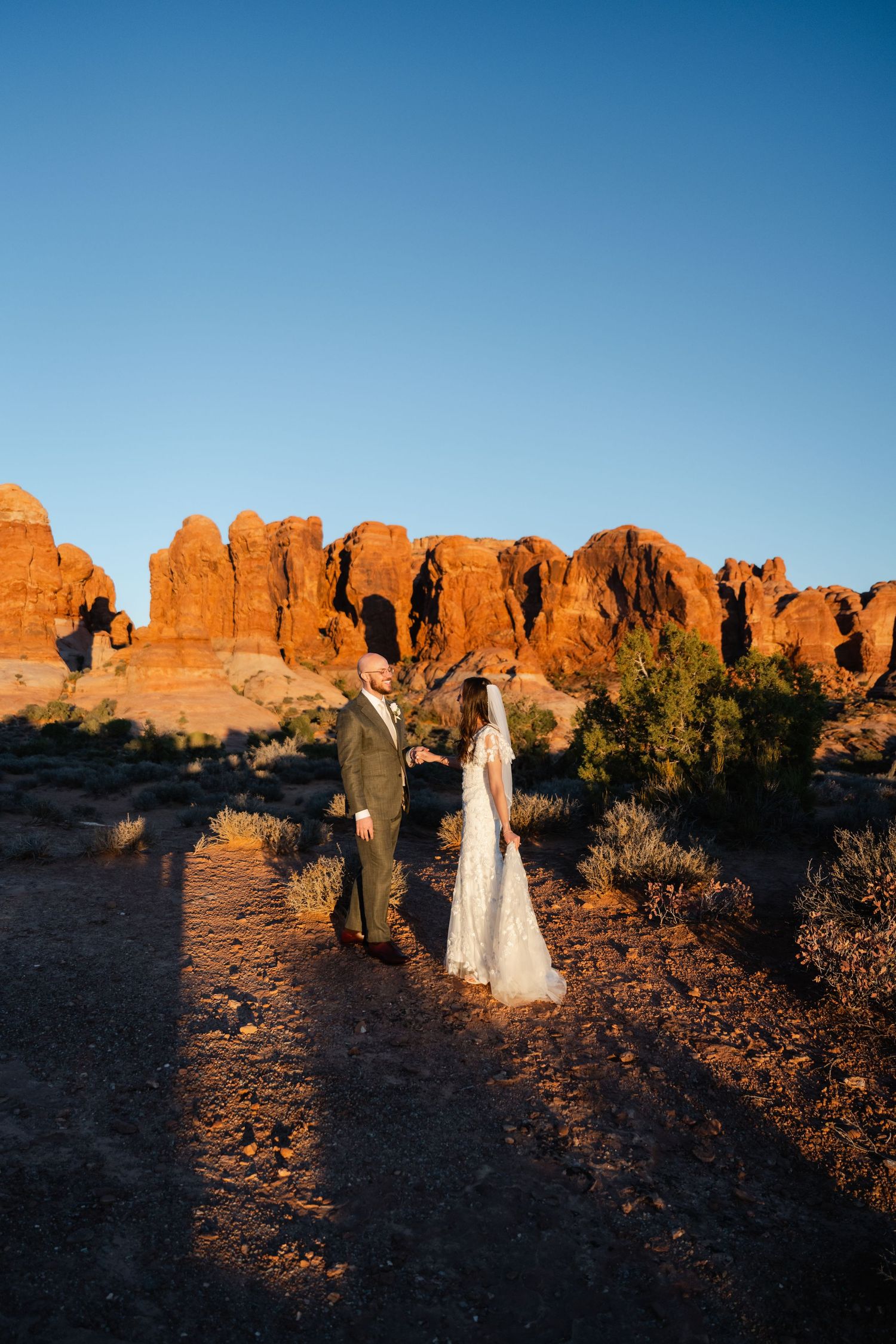Silhouettes against desert sunset with dramatic red rock formations in Arches National Park.
